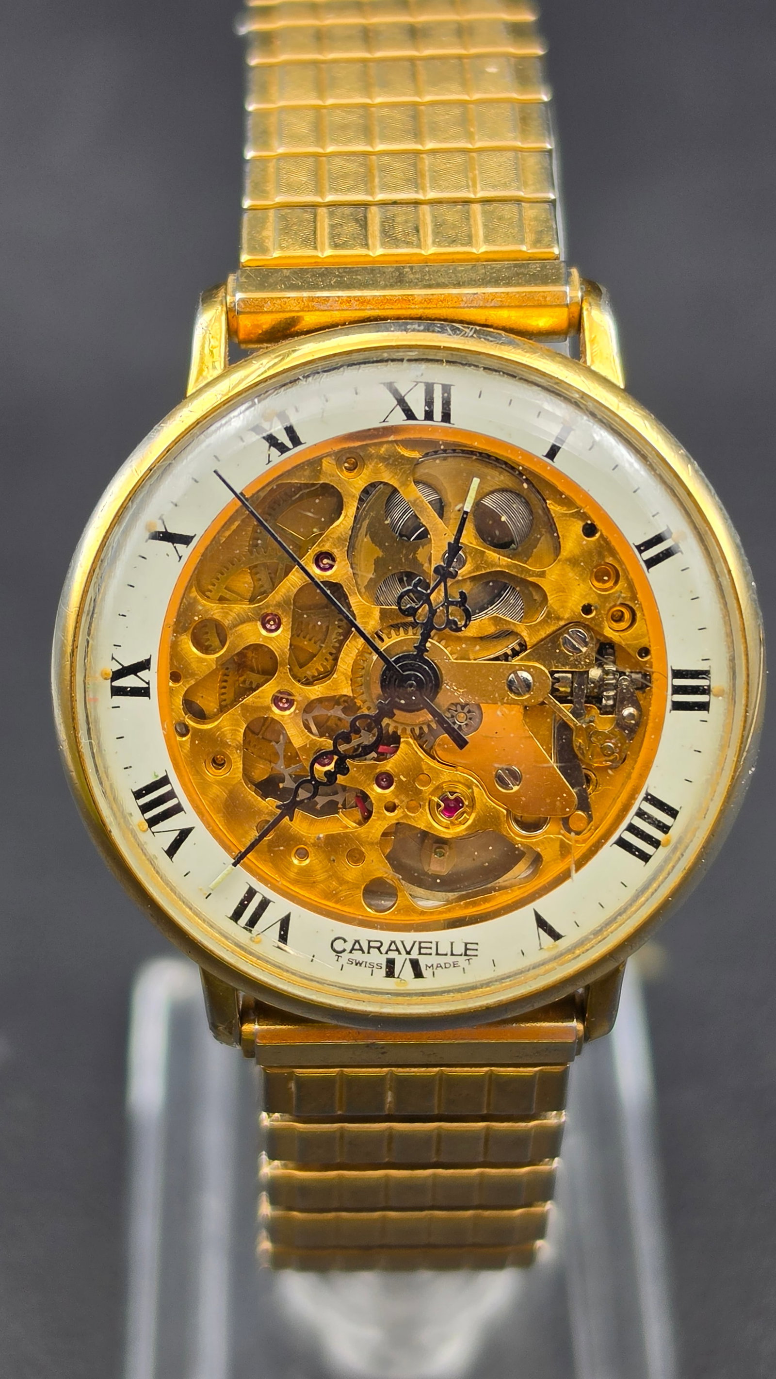 Vintage Caravelle Skeleton Watch Swiss Made Reference N8 Gold Tone Roman Numeral Dial: This is a vintage Caravelle skeleton watch, reference N8. The dial has a white chapter ring with black Roman numerals and a printed minute track, signed CARAVELLE, T SWISS MADE T, at the bottom. The c