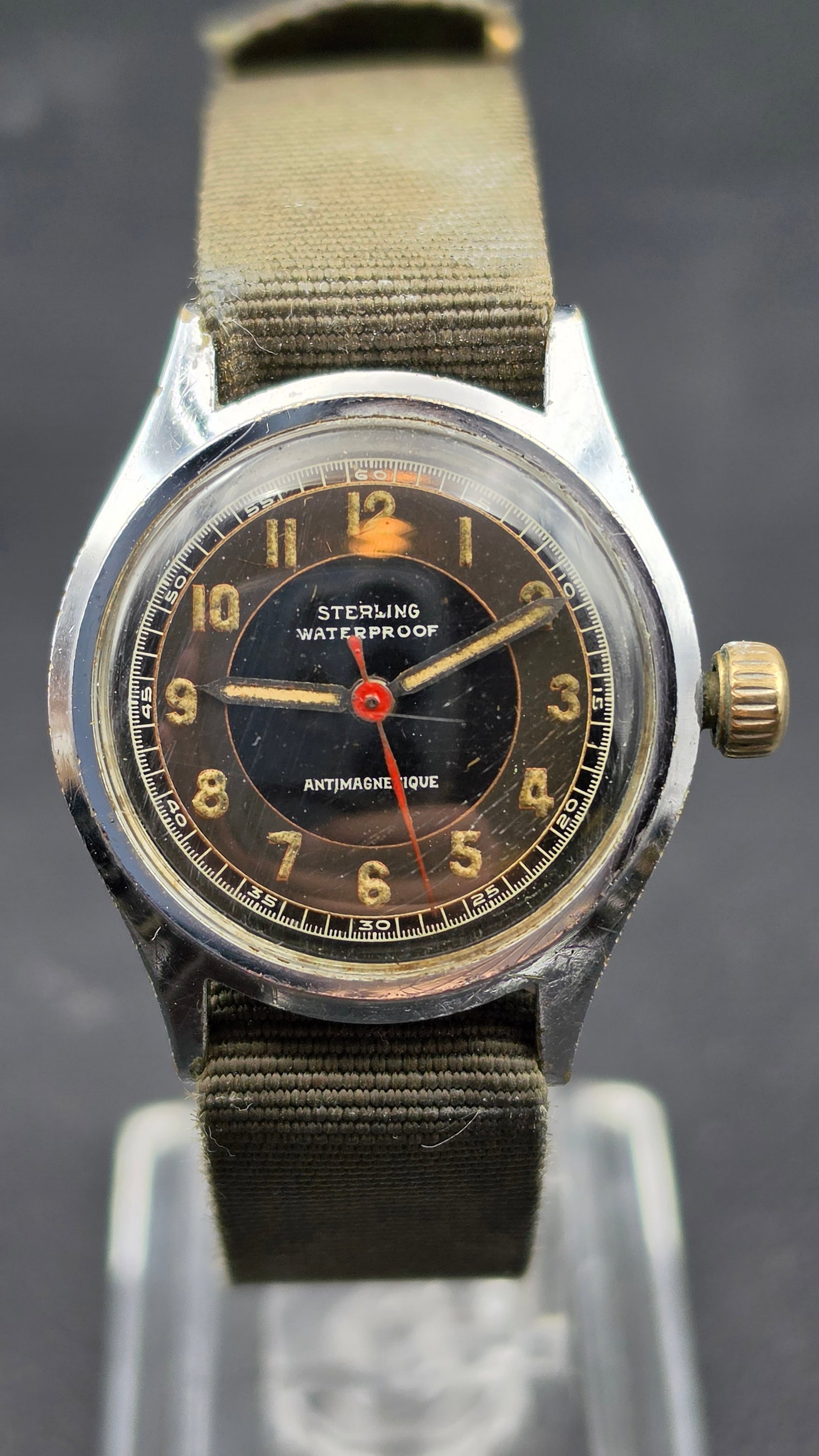 1940s Sterling Waterproof Antimagnetique Swiss Military Style Watch Running: This is a vintage Sterling Waterproof watch with a black dial signed Sterling, Waterproof, and Antimagnetique in white text. The dial features luminous gold tone Arabic numerals, luminous gold tone ho