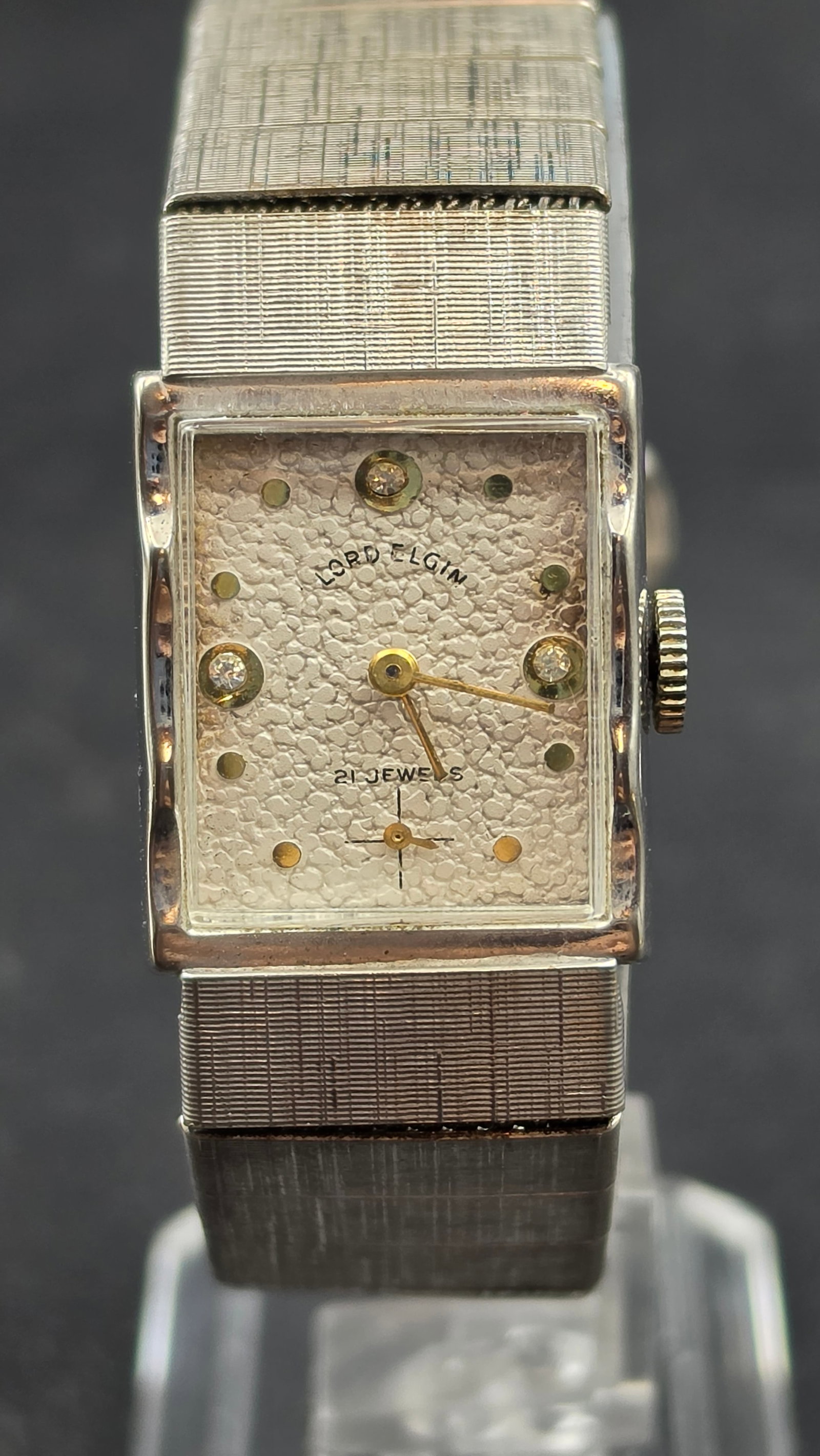 1950s Lord Elgin Cal. 670 21 Jewel Diamond Accent White Gold Filled Ladies Watch: This is a Lord Elgin ladies' wristwatch with a rectangular case in white gold filled metal and an integrated textured "linen" finish expansion bracelet. The dial is signed Lord Elgin, 21 Jewels, with 