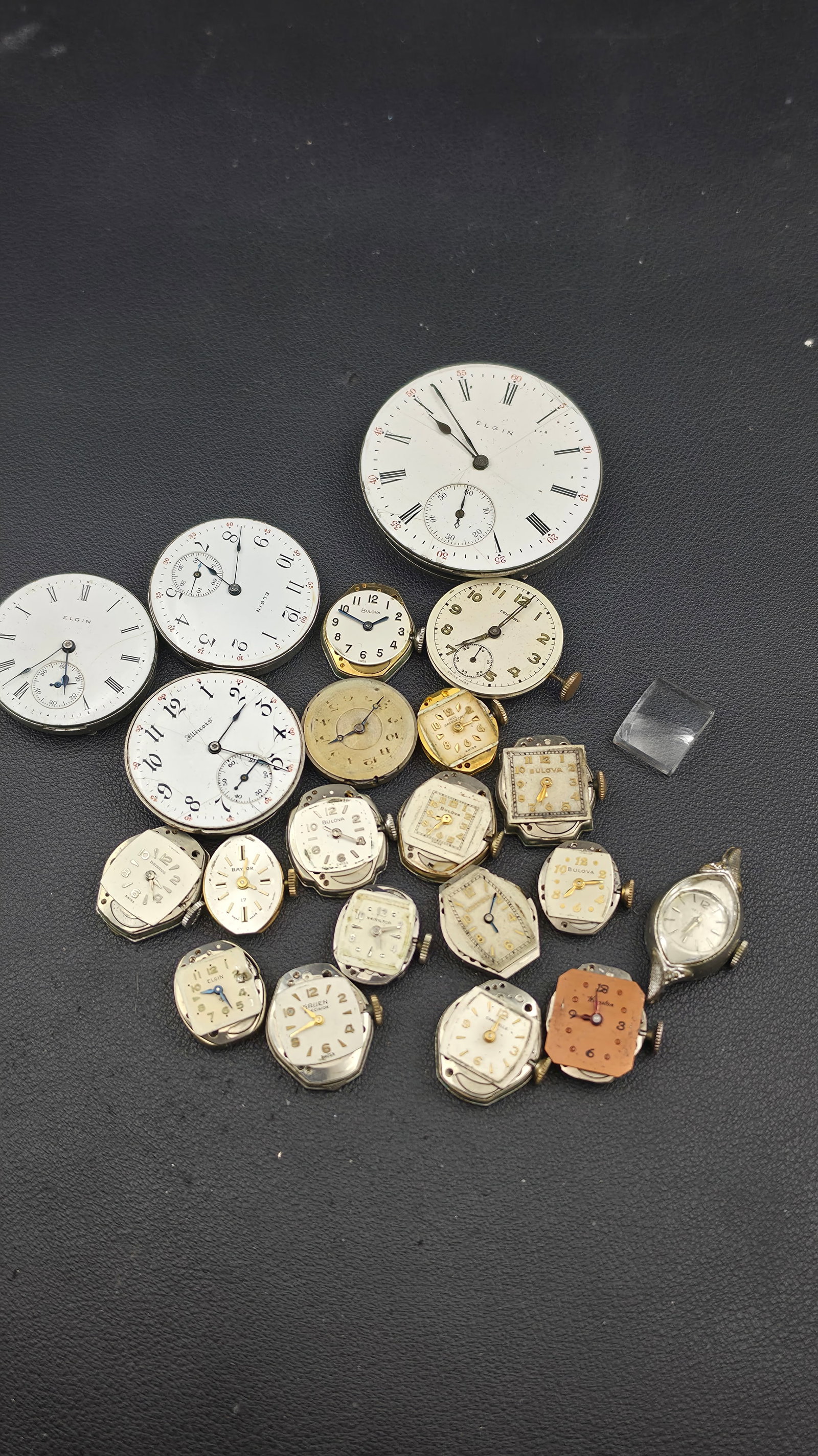 Early 1900s-1950s Elgin, Illinois, Bulova, and Other Brands Watch Movements Parts Lot, Untested: This large lot consists of over twenty loose watch movements and dials, mostly separated from their cases, offered together as parts or for restoration. Pocket watch movements include several Elgin 15
