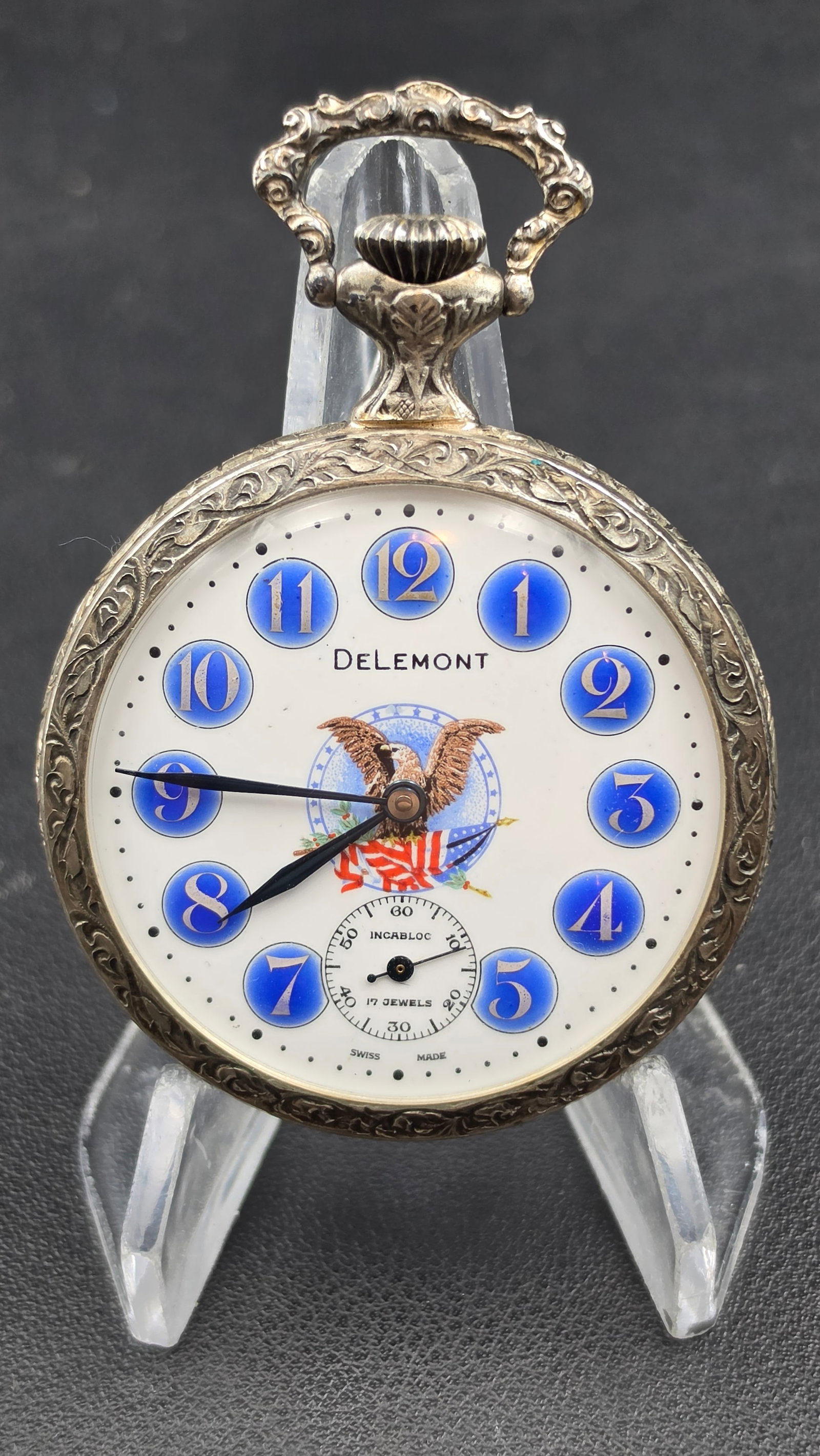 Arnex John F Kennedy Memorial Pocket Watch, Delemont Dial, 17 Jewels, 1970s: This commemorative pocket watch has a base metal case measuring 50.26mm, engraved overall with scrolling foliate motifs on the bezel, and a case back embossed in relief with a profile portrait of John