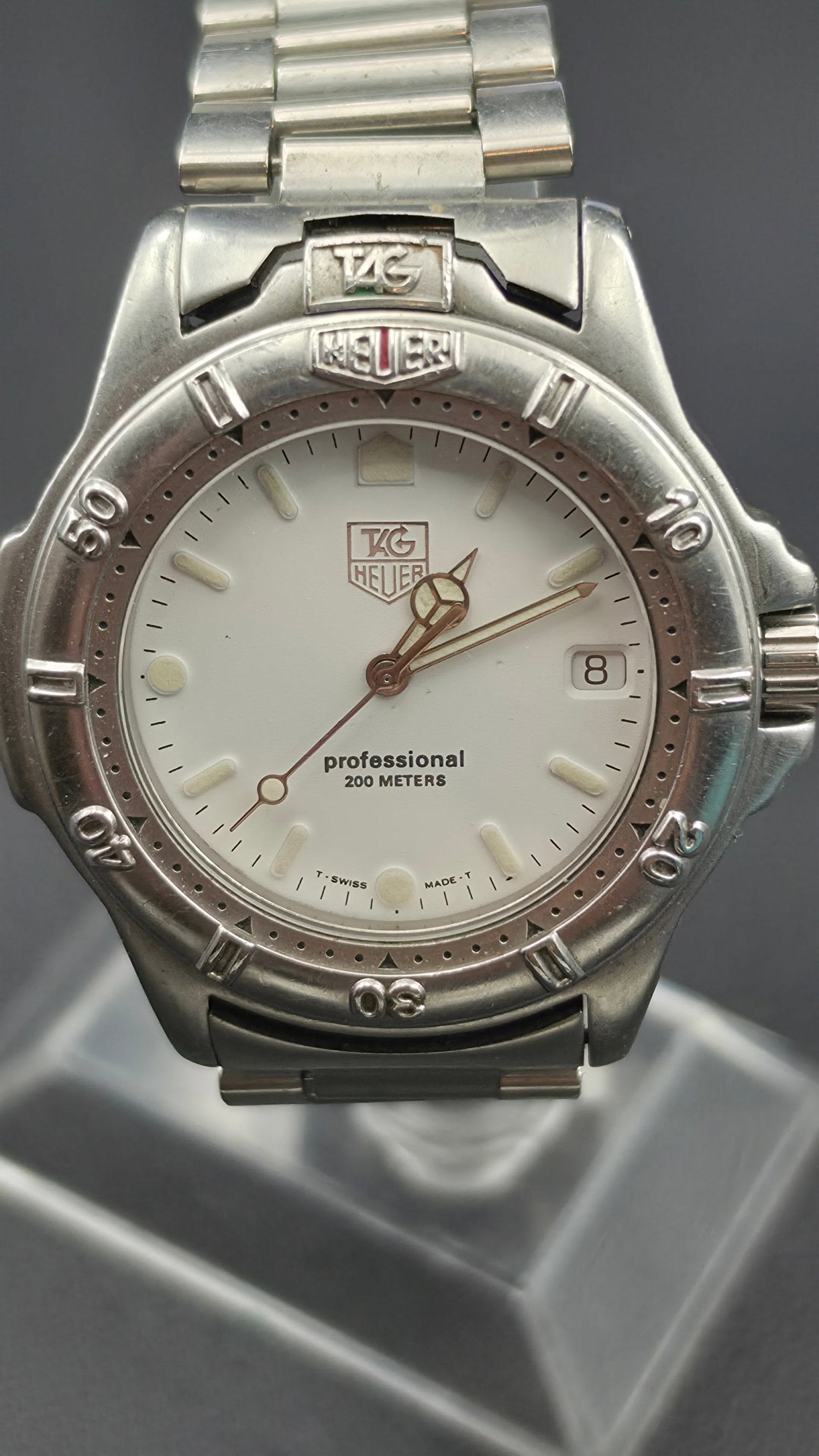 Vintage TAG Heuer 2000 Series Professional 200 Meters White Dial New Battery Running: This TAG Heuer 2000 Series wristwatch has a white dial signed TAG Heuer, Professional, 200 Meters, T Swiss Made T, with a date window and unidirectional rotating bezel, on the original all stainless s
