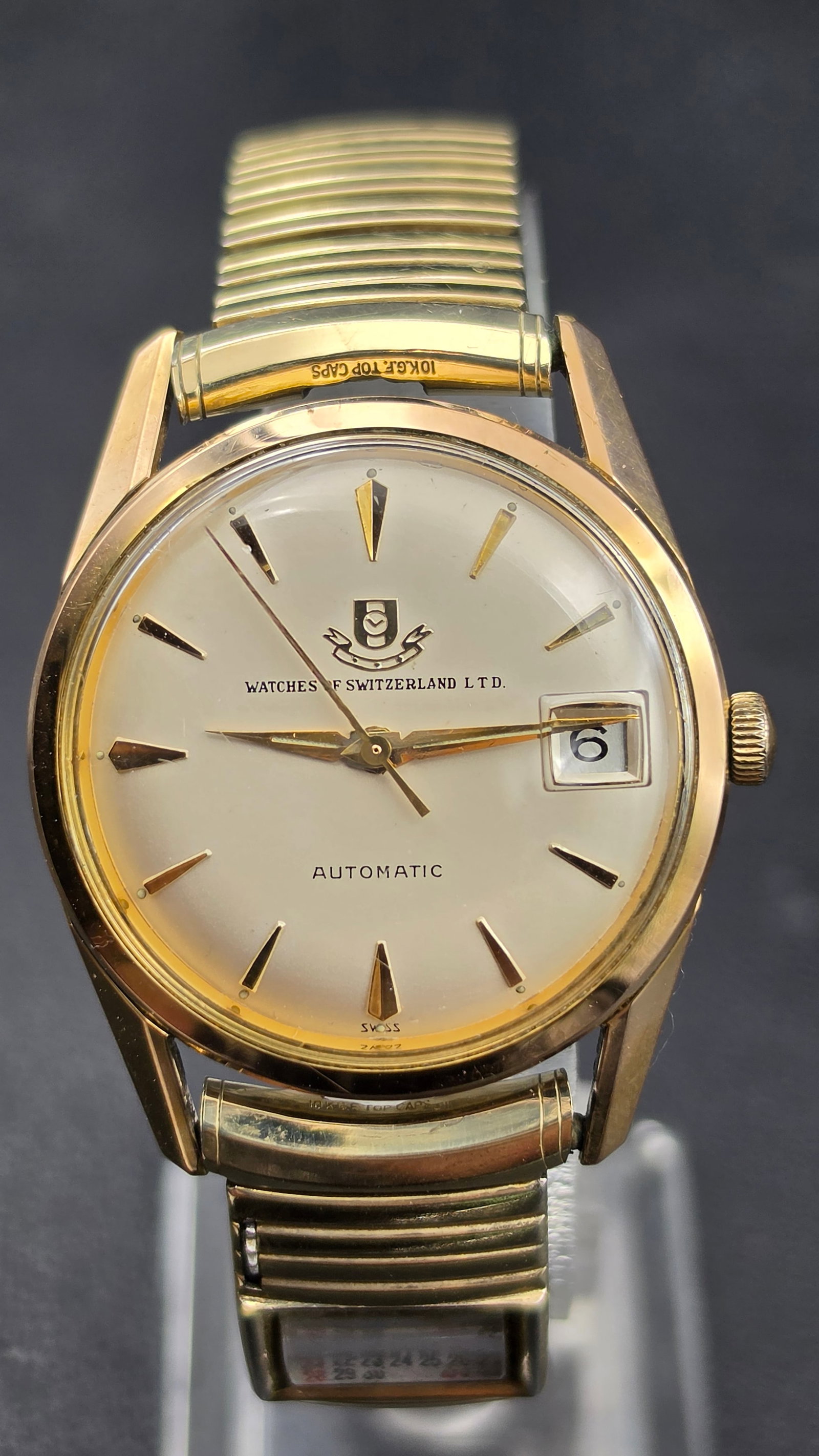 Vintage Watches of Switzerland Ltd. Automatic Date Watch 10K GF Top Caps Running: This is a vintage automatic wristwatch retailed by Watches of Switzerland Ltd., featuring a silvered dial with applied dagger-style hour markers, dagger hands, and a date window at 3 o'clock, signed W