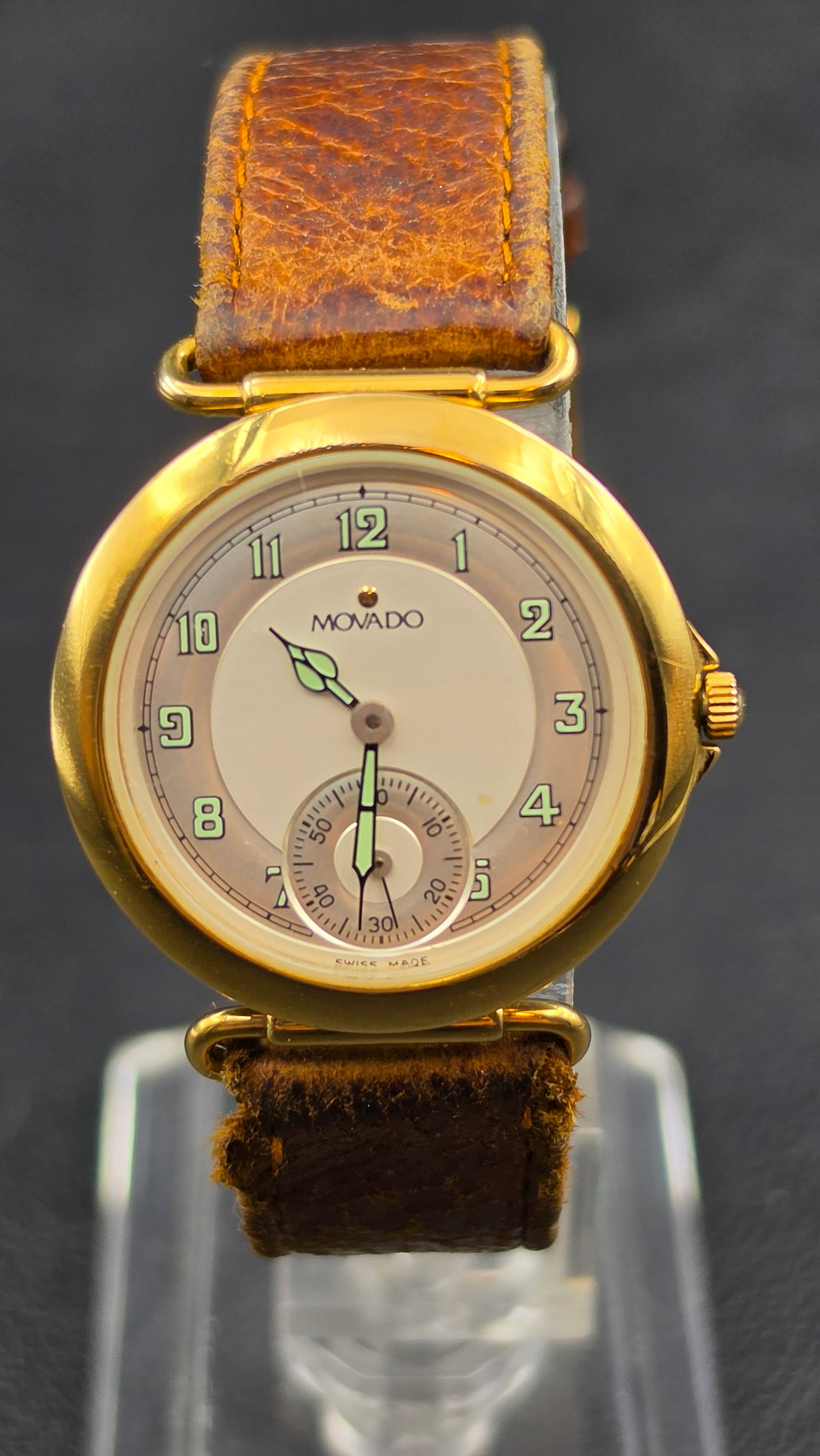 Vintage Movado ESQ Quartz Watch, Swiss Made, Gold Tone Case: This vintage Movado wristwatch features a two-tone cream dial signed "Movado," with green luminous Arabic numerals, a small seconds subdial at 6 o'clock, and "Swiss Made" printed at the bottom. The go