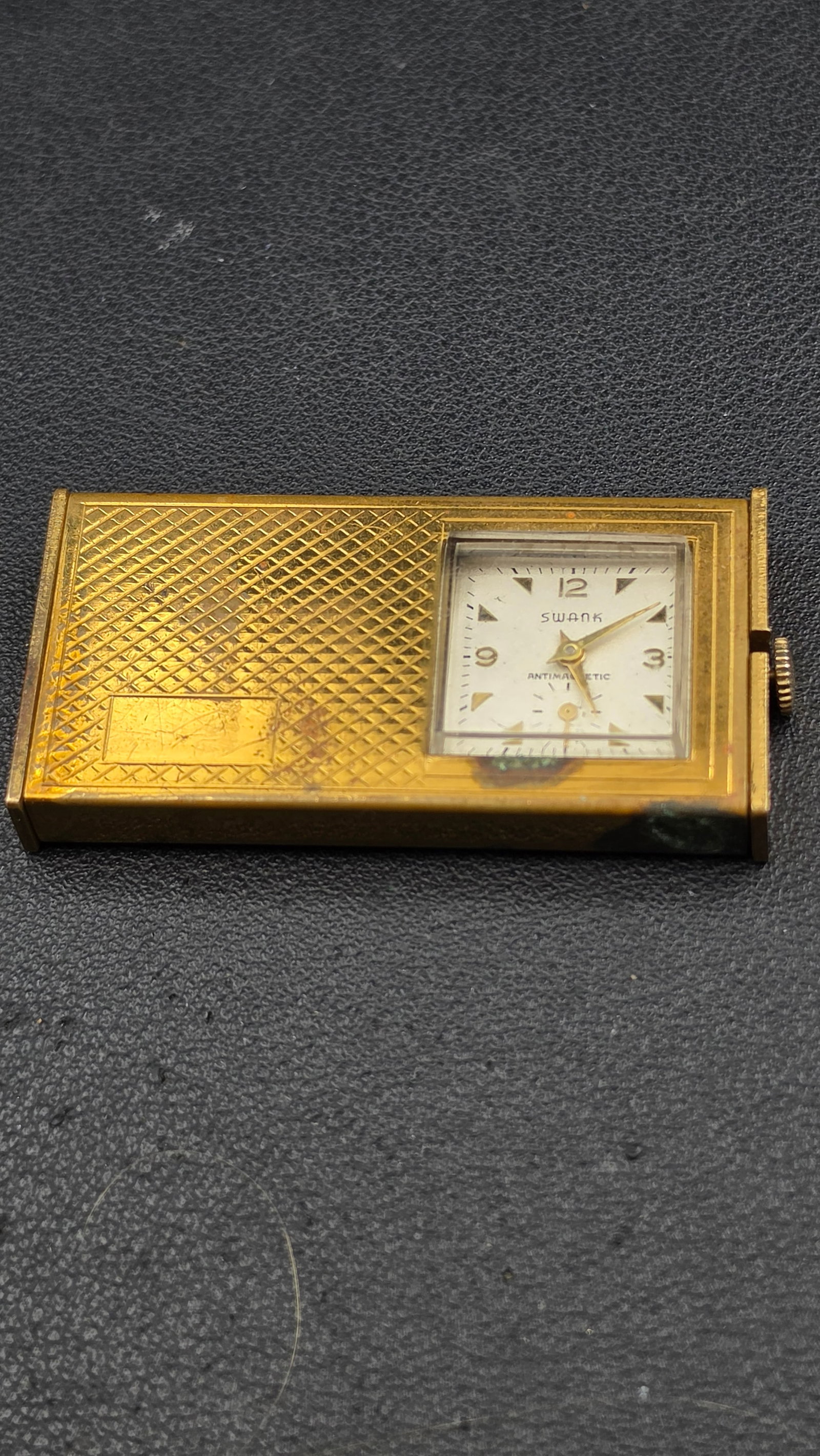 Vintage Swank Antimagnetic Folding Pocket Watch Gold Tone Case: This is a Swank folding pocket watch, signed Swank Antimagnetic on the dial with Arabic numerals and triangular hour markers. The case is gold-tone with an engine-turned pattern and a blank engraving 