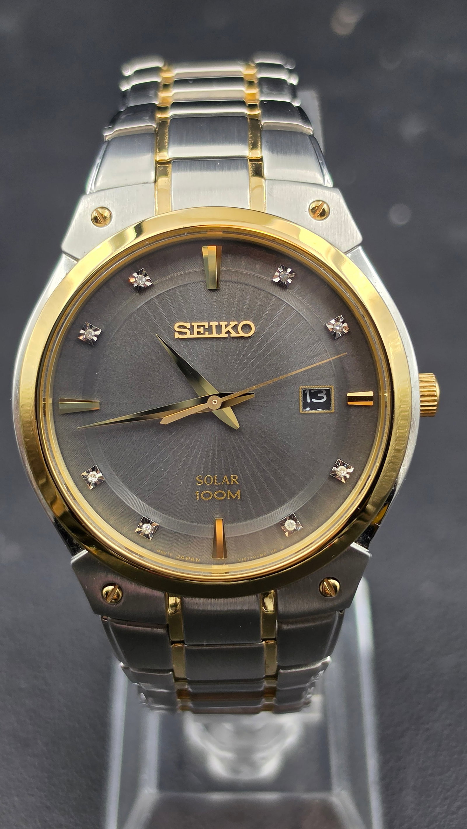 Seiko Solar Wristwatch, Ref V167, Diamond Markers, Two-Tone, NOS, Box & Papers: This Seiko Solar wristwatch, caliber V167, features a gray sunburst dial signed Seiko Solar 100M with diamond hour markers, gold-tone dagger hands, and a date window at 3 o'clock, in a two-tone stainl
