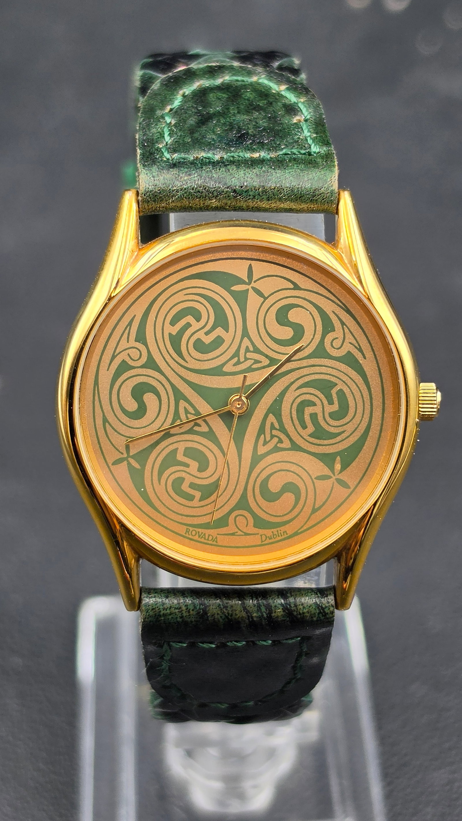 Rovada Dublin Celtic Triskele Design Quartz Watch Green Braided Leather Strap NOS: This is a Rovada Dublin quartz watch featuring a gold-tone dial engraved with a Celtic triskele spiral design against a green background, signed Rovada Dublin. The case back is stamped stainless steel