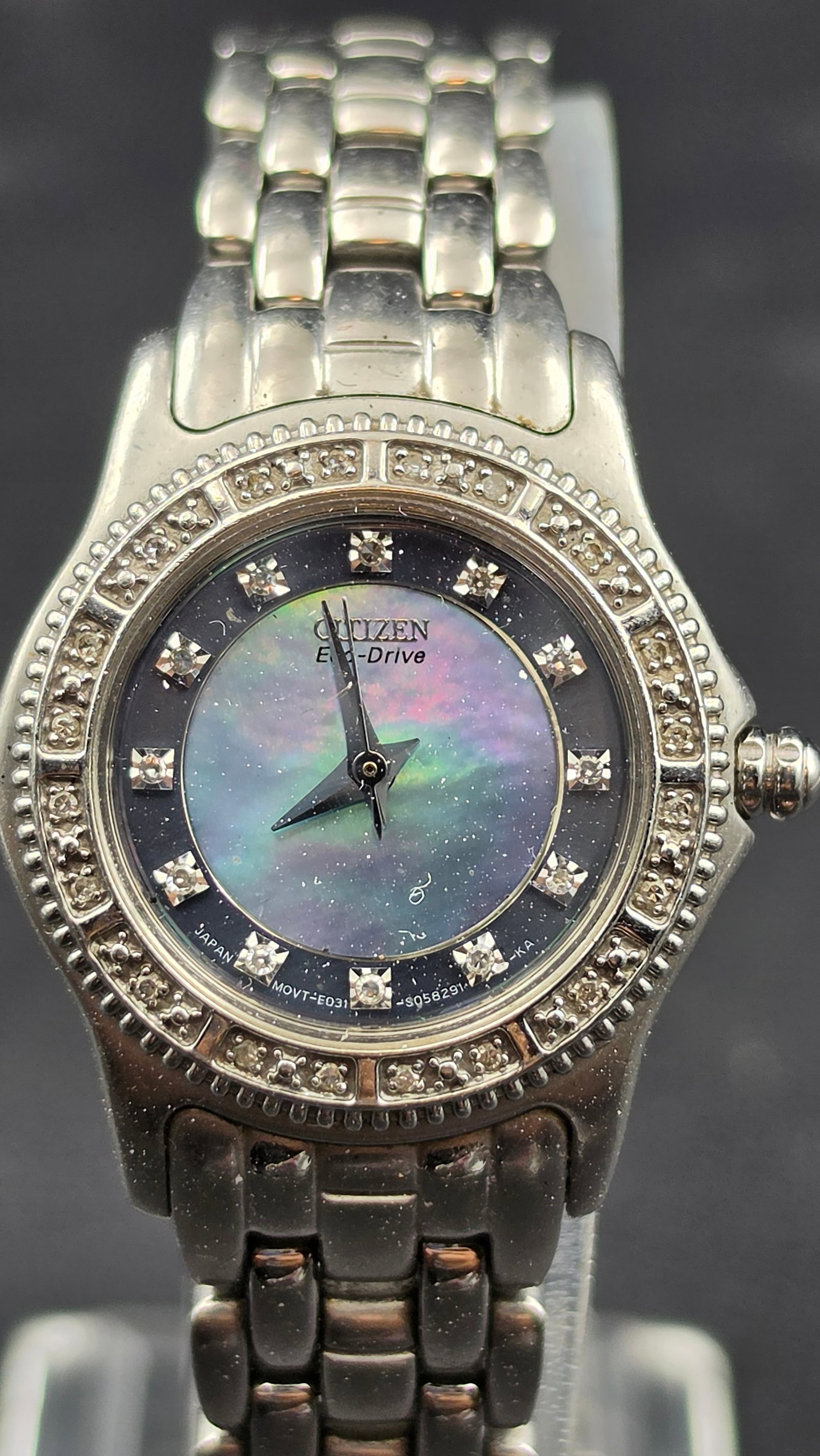 Citizen Eco-Drive Diamond Bezel Mother of Pearl Ladies Watch E031: This is a Citizen Eco-Drive ladies watch featuring a black mother of pearl dial with diamond hour markers, set beneath a sapphire crystal and framed by a diamond-set bezel. The case back is signed Cit