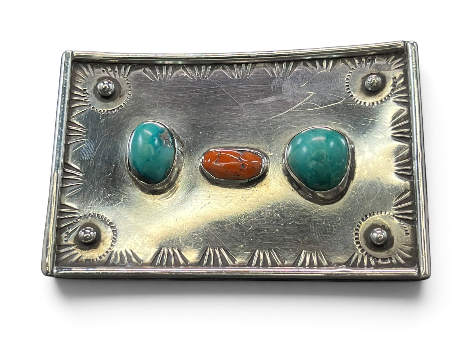 66g Navajo Sterling Silver Belt Buckle with Turquoise and Coral, Stamped Concho Corners: Sterling silver Navajo belt buckle, rectangular in form with a gently curved, concave profile that follows the body’s natural line when worn. The face is bordered on all four sides by a continuous h