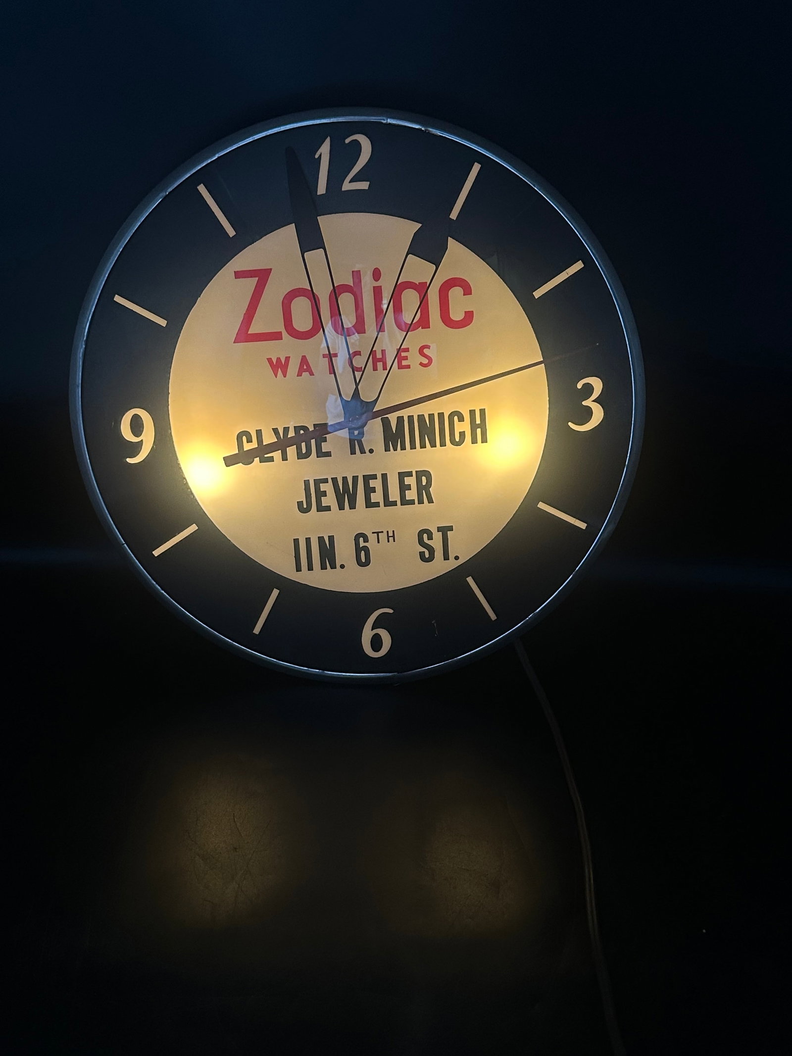Vintage Zodiac Watches Lighted Advertising Wall Clock: Mid-century illuminated Zodiac Watches advertising wall clock made for Clyde R. Minich Jeweler. Features a convex glass face, bold Zodiac branding, dealer lettering, and a metal case with internal lig