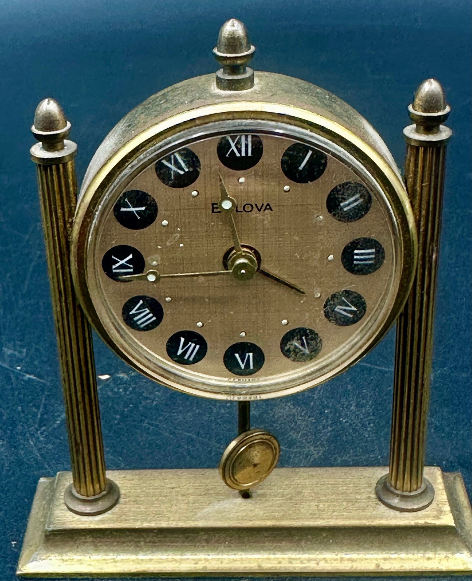 Vintage Bulova Swiss 8-Day Alarm Desk Clock: Vintage Bulova mechanical desk/travel clock featuring a gilt-tone architectural case with fluted columns, Roman numeral dial, center alarm hand, and pendulum-style decorative element. Dial appears mar