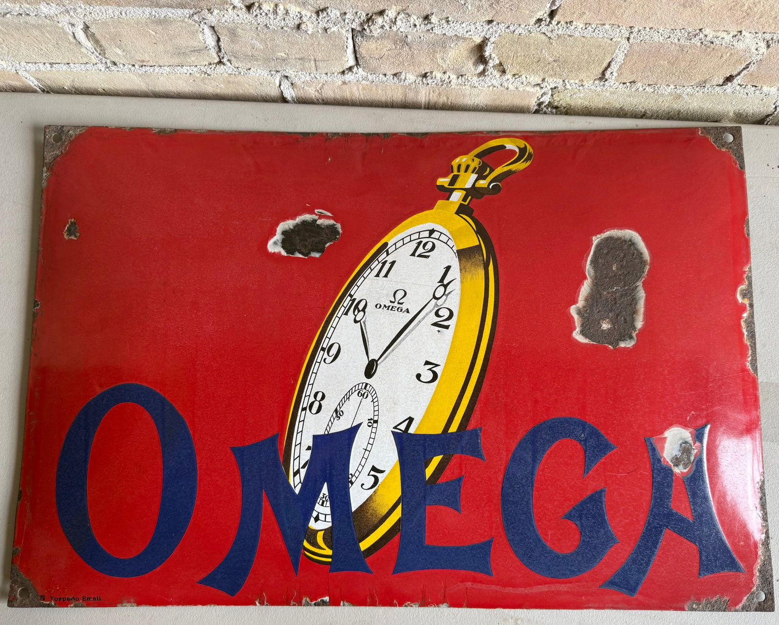 1920’s Vintage Omega Porcelain Enamel Advertising Sign by Torpedo Email (Frankfurter Em: Vintage Omega pocket watch porcelain enamel advertising sign from around the 1920s, featuring a red background and a large gold pocket watch graphic. The sign exhibits typical signs of age, including 