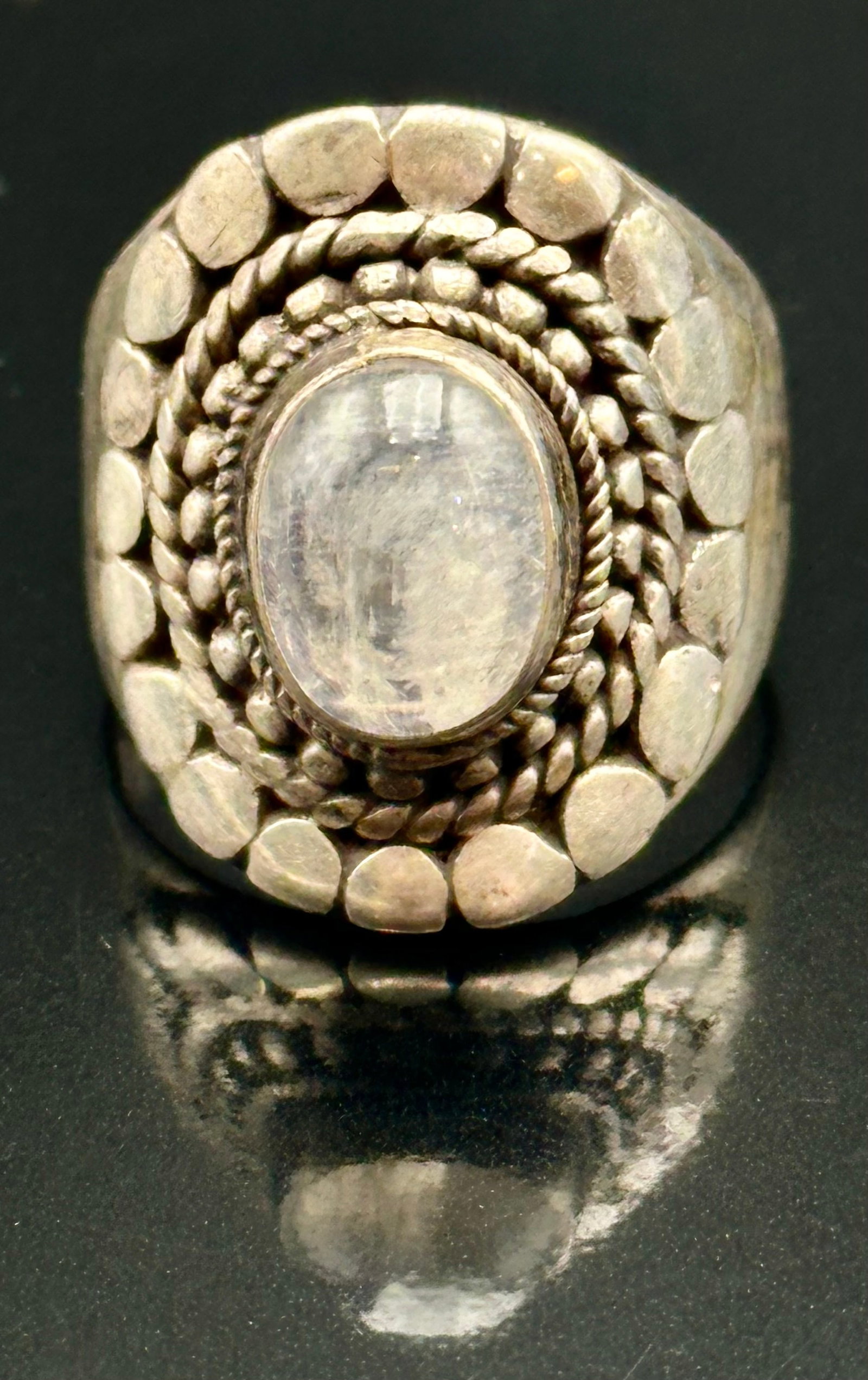 7g Vintage Sterling Silver Rainbow Moonstone Statement Ring: Vintage sterling silver ring with an oval rainbow moonstone showing a soft blue flash. Detailed with silver beads, twisted rope and raised accents on a wide band. Shows patina and light vintage wear. 