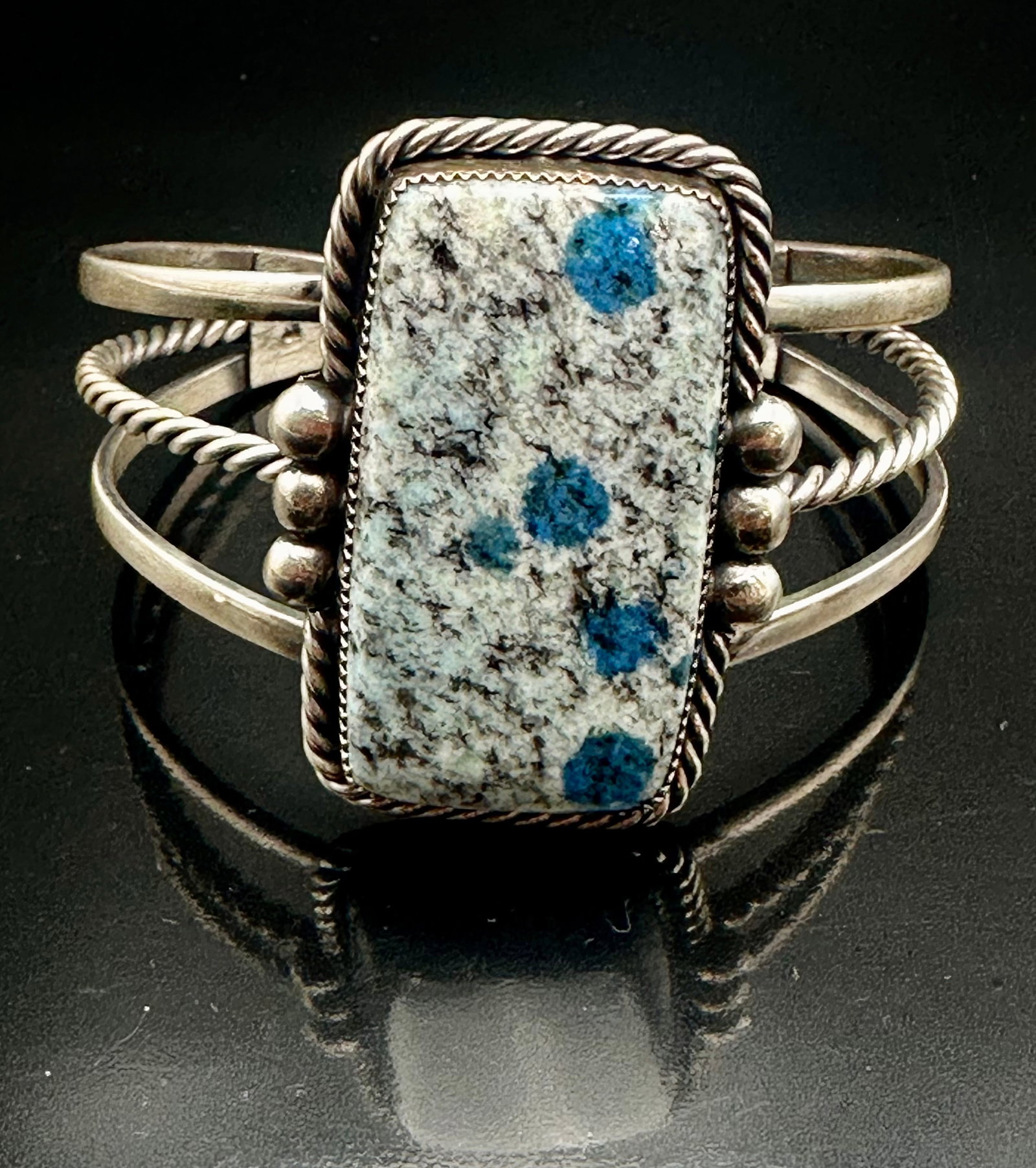 50g Native American Sterling Silver K2 Stone Cuff Bracelet: Handmade Native American sterling silver cuff bracelet with a large rectangular K2 granite stone featuring blue azurite spots. Decorated with twisted wire and silver bead details. Signed with an artis