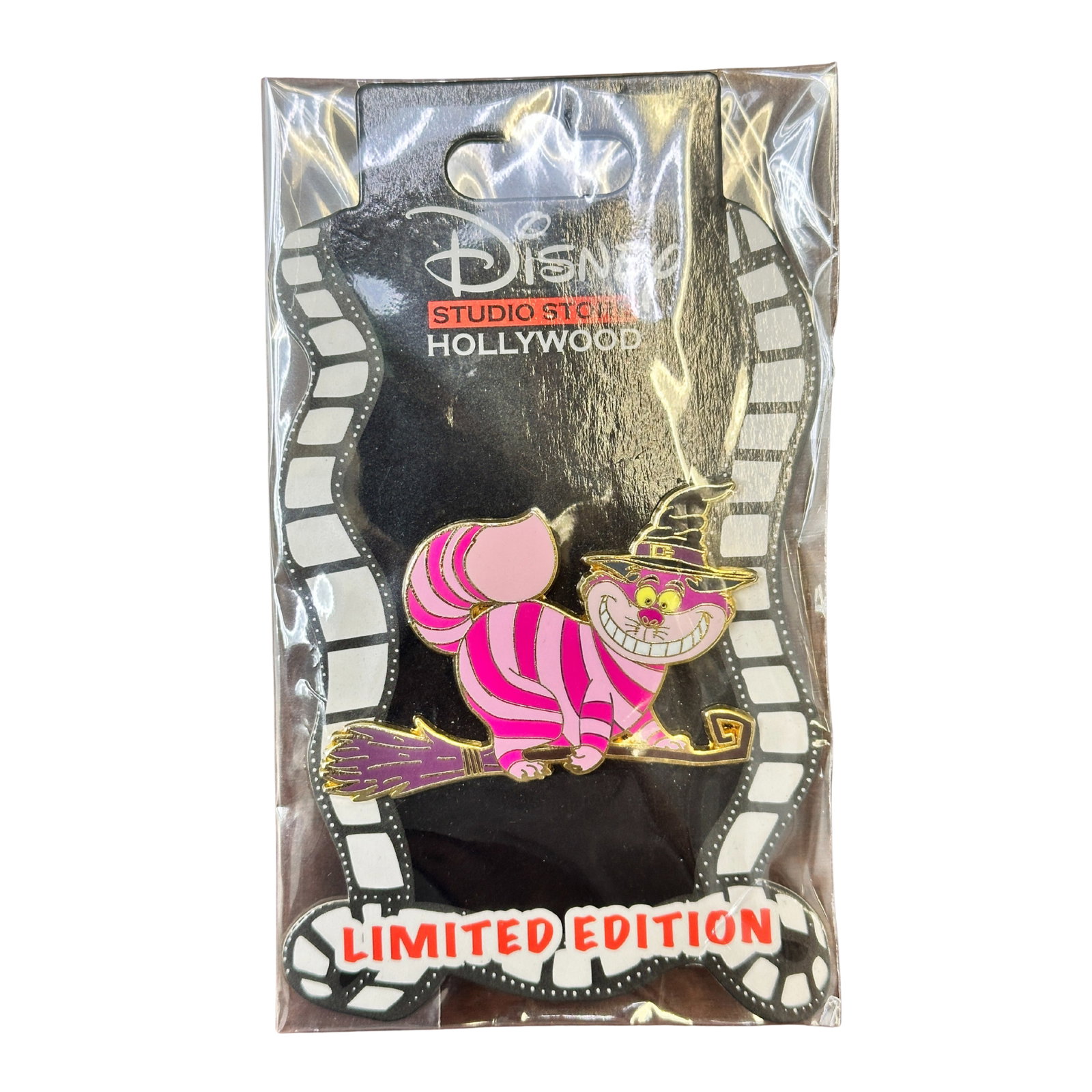 Disney DSSH Alice In Wonderland Cheshire Cat On A Broom Pin: Disney DSSH Alice In Wonderland Cheshire Cat On A Broom Pin. This pin features the Cheshire Cat from Alice in Wonderland. He is light pink and purple with yellow eyes, and standing on a broom. He is w