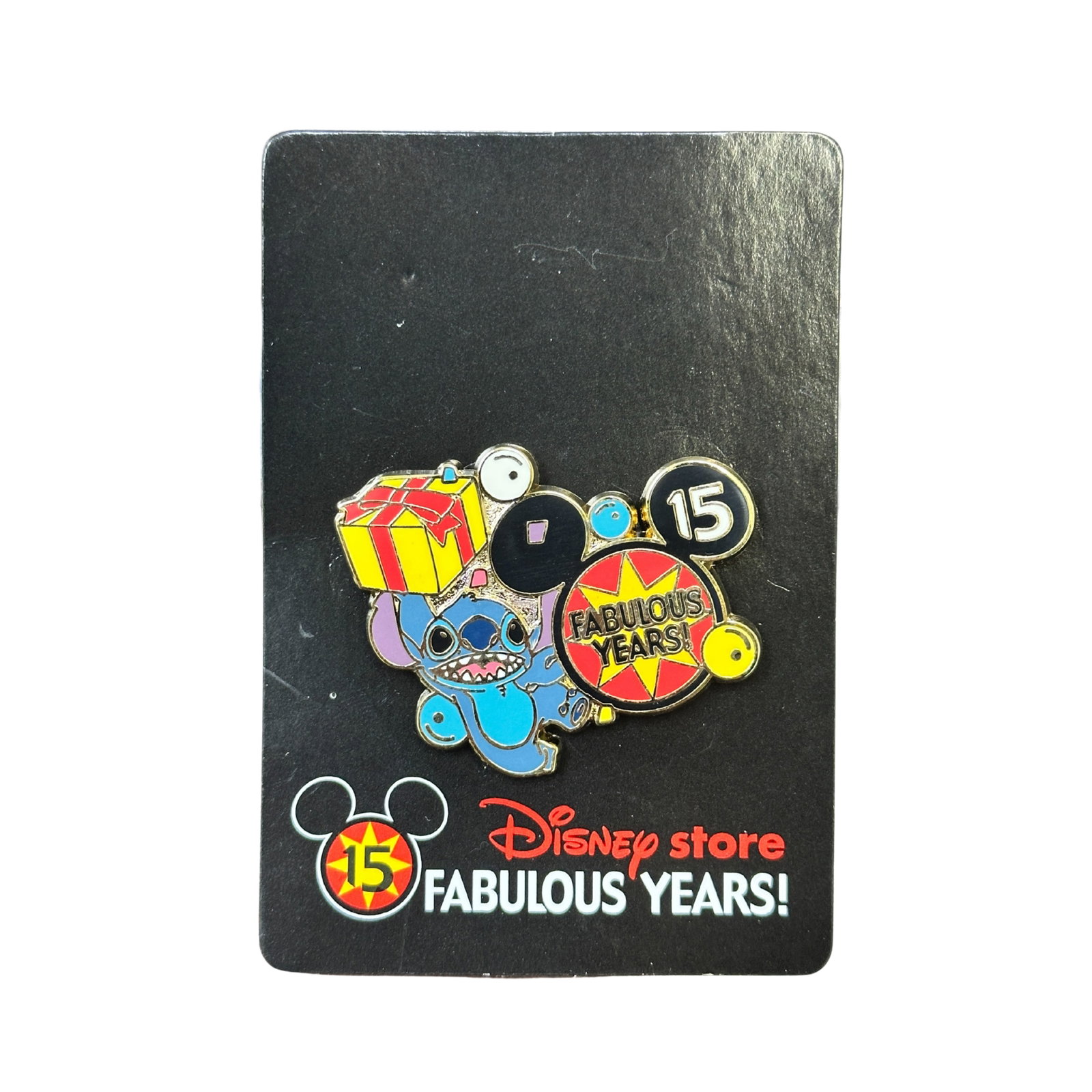 Disney JDS Lilo & Stitch 15 Fabulous Years Pin: Disney JDS Lilo & Stitch 15 Fabulous Years Pin. This pin features Stitch from “Lilo and Stitch”. Stitch is next to a Mickey Mouse head icon and is putting a present on the head. The Mickey hea