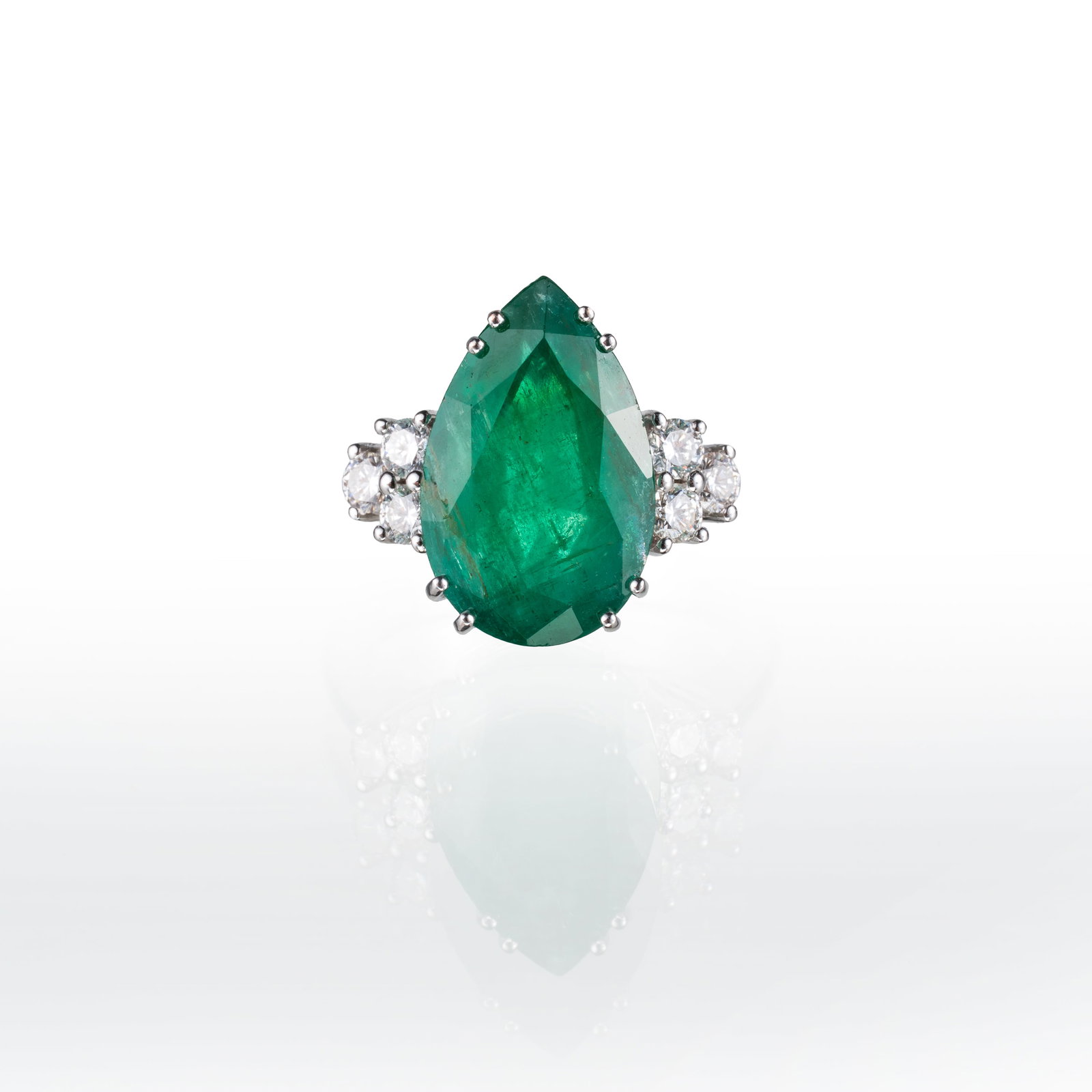 18 KT WHITE GOLD RING WITH AN EMERALD AND BRILLIANT-CUT DIAMONDS: An 18-carat white gold ring featuring a teardrop-shaped emerald measuring 9.92 x 15.68 mm and 6 brilliant-cut diamonds with an estimated total weight of approximately 0.24 carats. Width: 16.26 mm thic
