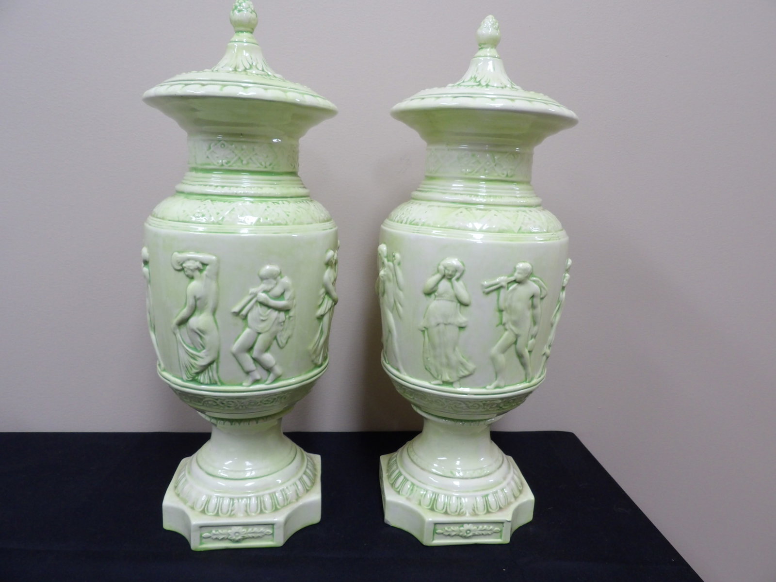 pair of green glazed ceramic tall urns with relief figures: Approx. 20 inches height. Lids appear to be adhered to urns.