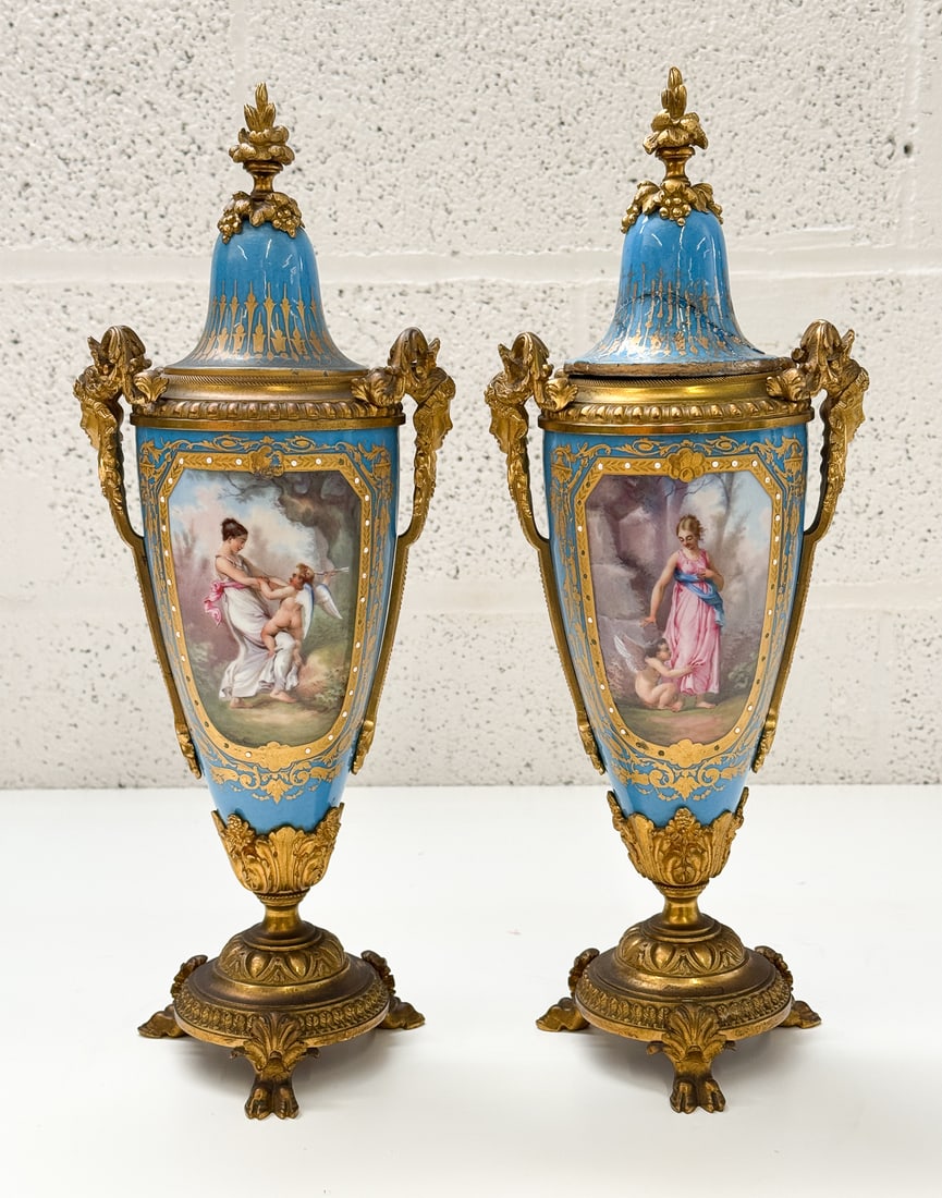 Petite Pair of Sevres Style Lidded Urns: Early 20th century. Each 16 inches high. 1 lid has been repaired. See photos for condition.