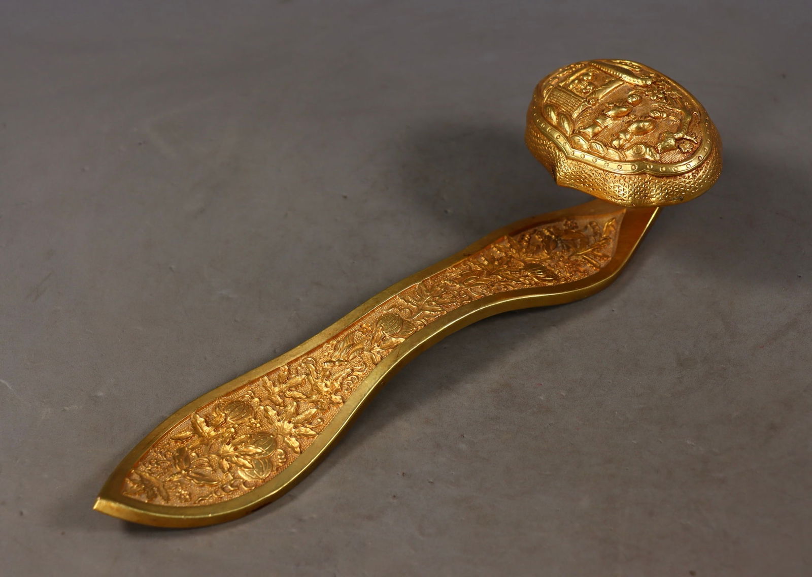 An Exquisite Gilt Bronze Character and Story Pattern Flower and Fruit Pattern Ruyi: An Exquisite Gilt Bronze Character and Story Pattern Flower and Fruit Pattern Ruyi Qing Dynasty, China Size:6.5cmx25cmx8cm Weight:594g (The Dimensions Of All Batches Are Manually Measured.If You