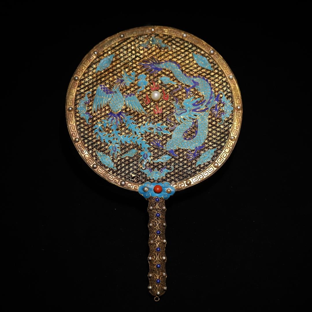 A silver-gilt filigree dotted emerald dragon and phoenix pattern inlaid treasure fan of the Qing: The silver gilt filigree dotted emerald dragon and phoenix pattern inlaid treasure group fan of the Qing Dynasty Size:L: 34x21.2cmW:0.3214kg (The Dimensions Of All Batches Are