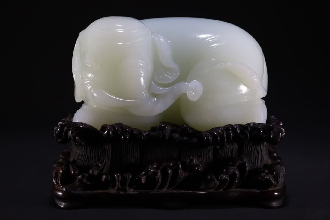 A white jade reclining elephant ornament of the Qing Dynasty: Qing Dynasty white jade reclining elephant ornament is carved from Hetian white jade, the body of the reclining elephant is round and thick, the facial features are round and gentle, and the texture i