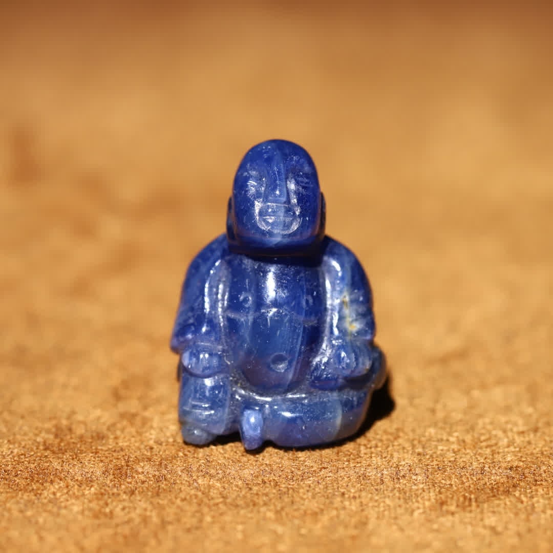 A sapphire personal Buddha carving: Sapphire Personal Buddha Carving: Made from a whole natural sapphire carved in a round, the stone body is a rich and deep indigo with natural mineral patterns and colored bands, giving it a lustrous