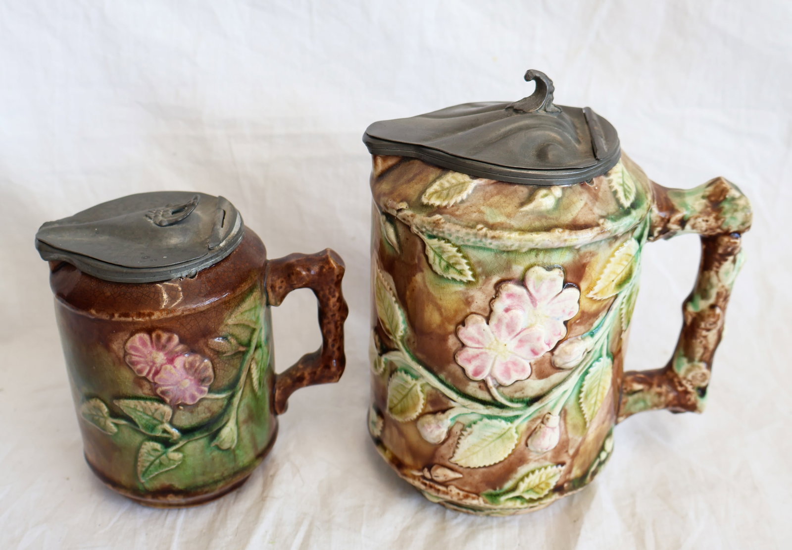 Lot of Two Majolica Pitchers with Pewter Lids: Large: 6 3/4" x 5 3/4" with handle Small: 4 1/2" x 4 1/4" with handle Gurley Auction Company provides In House Packing and Shipping and strive to keep costs as reasonable as possible. Please