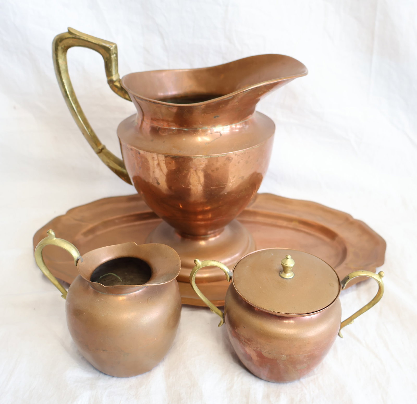 Four Piece Set of Signed Copper; Pitcher, Creamer, Sugar Bowl, and Tray: Signed "PG Mexico Plateado" Pitcher: 8 1/2" x 8 1/2" with handle Tray: 8" x 13 3/4" Creamer: 4" x 4 1/2" with handle Sugar: 3 1/2" x 5 1/2" with handles Gurley Auction Company provides In House Packin