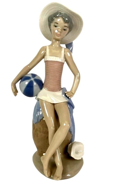LLADRO SUMMER 1984-99 PORCELAIN FIGURINE 5219G: LLADRO SUMMER 1984-99 PORCELAIN FIGURINE 5219GLladro porcelain figurine titled Summer Girl with Beach Ball, model 5219. Depicts a girl in a swimsuit and sun hat holding a beach ball, leaning on a text