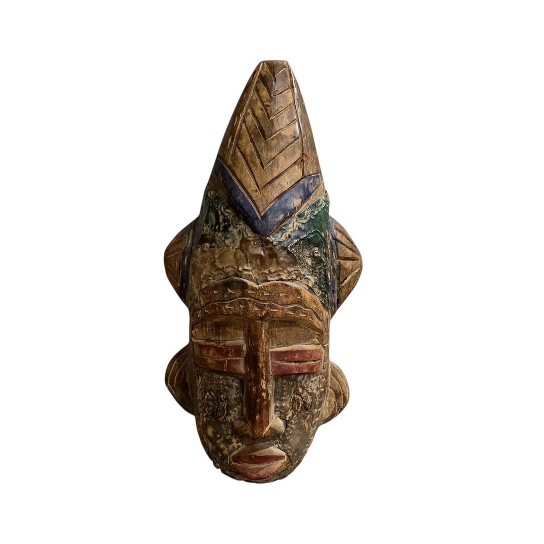 Mask - Africa - Carved African mask: Carved Wooden African mask Measuring 16 inches in length, featuring intricate design elements including a pointed crest and geometric patterns. The mask is adorned with metal accents and faint traces