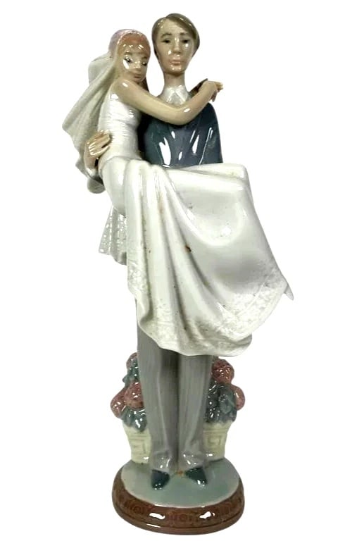 Lladro 01005282 5282 Over The Threshold Wedding Couple: Lladro 01005282 5282 Over The Threshold Wedding CoupleLladro porcelain figurine titled Over the Threshold, model number 5282. Depicts a groom carrying a bride, adorned with detailed floral baskets at 