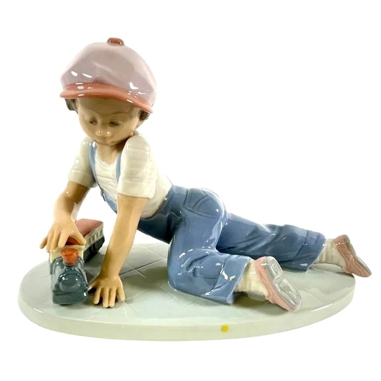 LLADRO ALL ABOARD 1992 SOCIETY 1992-95 PORCELAIN FIGURINE 7619G: LLADRO ALL ABOARD 1992 SOCIETY 1992-95 PORCELAIN FIGURINE 7619GLladro All Aboard #7619 porcelain figurine depicting a young boy in overalls playing with a toy train. Featuring soft pastel tones and in