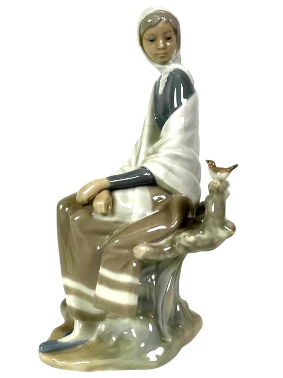 LLADRO NEW SHEPHERDESS 1969-85 PORCELAIN FIGURINE 4576G: LLADRO NEW SHEPHERDESS 1969-85 PORCELAIN FIGURINE 4576GLladro porcelain figurine titled 'New Shepherdess,' model number 4576. Depicts a seated shepherdess in a hooded wrap, holding a staff, with a bir