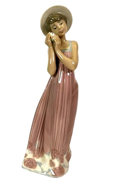 LLADRO CINDY 1990-98 PORCELAIN FIGURINE 5646G: LLADRO CINDY 1990-98 PORCELAIN FIGURINE 5646GLladro porcelain figurine titled Cindy (#5646), standing 8 inches tall. Depicts a young woman in a flowing pink dress adorned with floral details, holding 