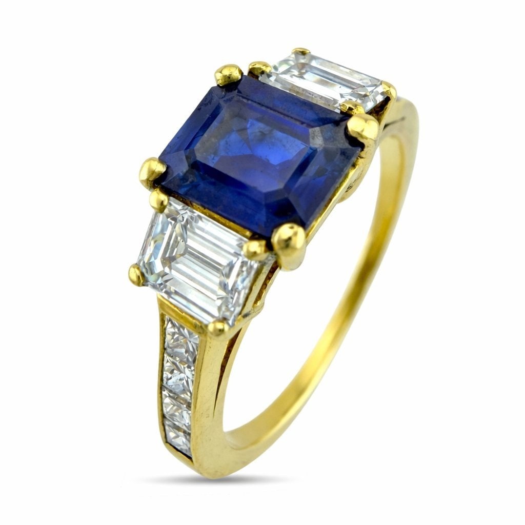 18K Yellow Gold 1.25ct Sapphire and 1ct Diamond Ring: 18K Yellow Gold 1.25ct Sapphire and 1.0ct Diamond Cocktail Ring A refined three stone composition showcasing a richly hued rectangular cut sapphire framed by crisp geometric diamonds. The clean lines 
