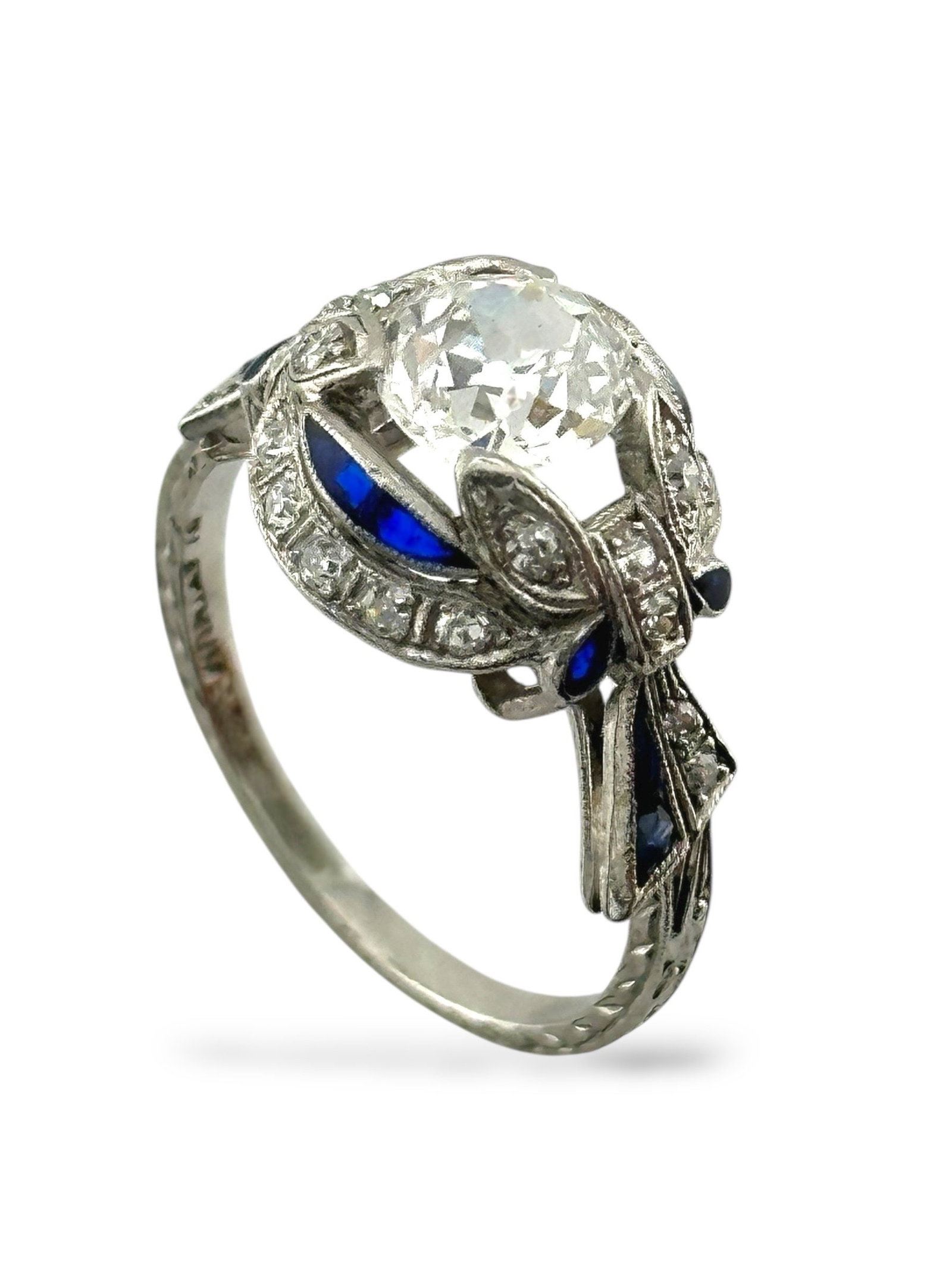 Art Deco Platinum Ring: Platinum Ring with 1 Carat Diamond, Sapphires, and Accent Diamonds A striking platinum ring showcasing a dazzling 1 carat center diamond framed by a graceful halo of natural sapphires and