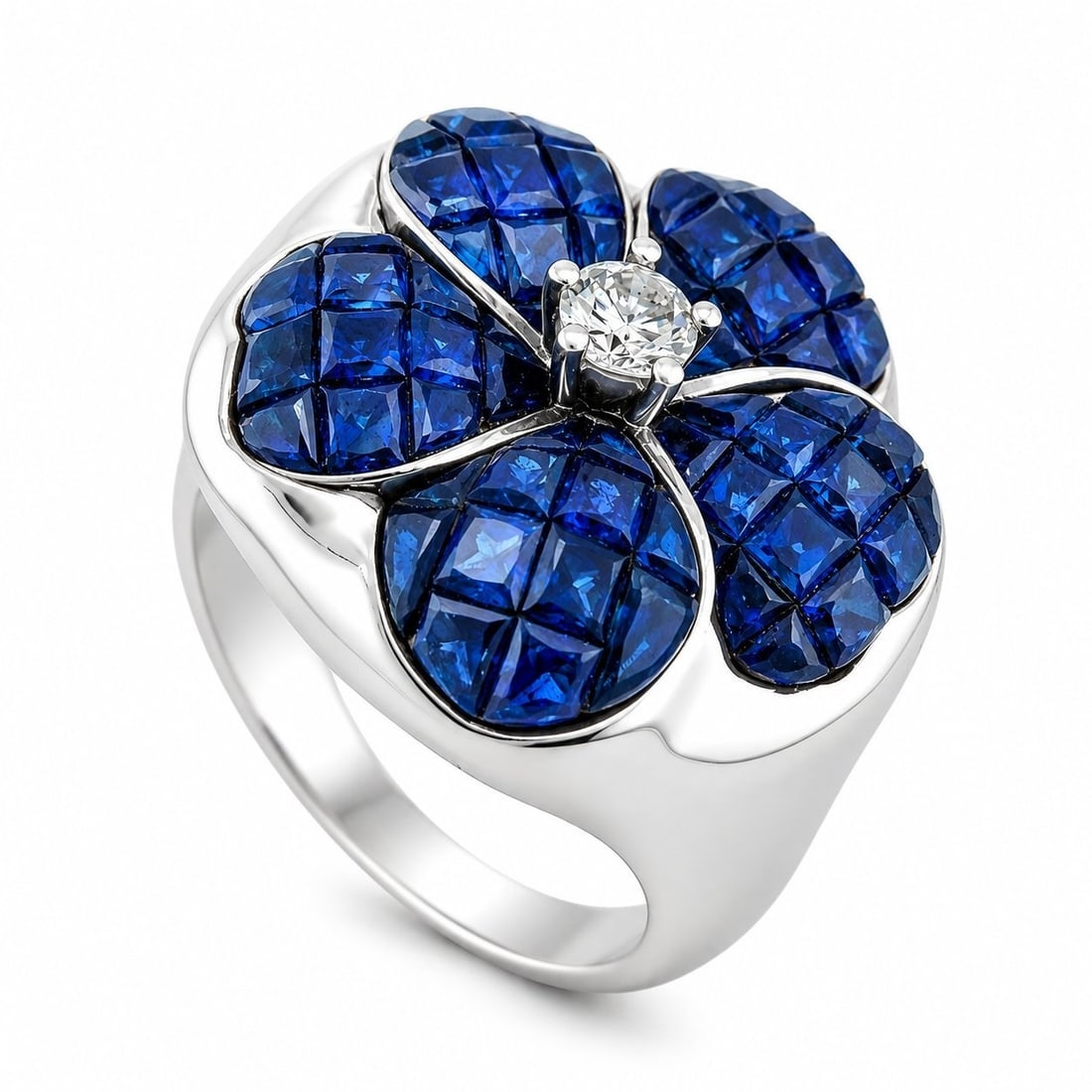 18K White Gold Diamond and Blue Sapphire Flower Ring: 18K White Gold Diamond and Blue Sapphire Flower Ring This elegant ring is crafted in 18 karat white gold and features a refined flower design centered with a round brilliant diamond. Square-cut blue s