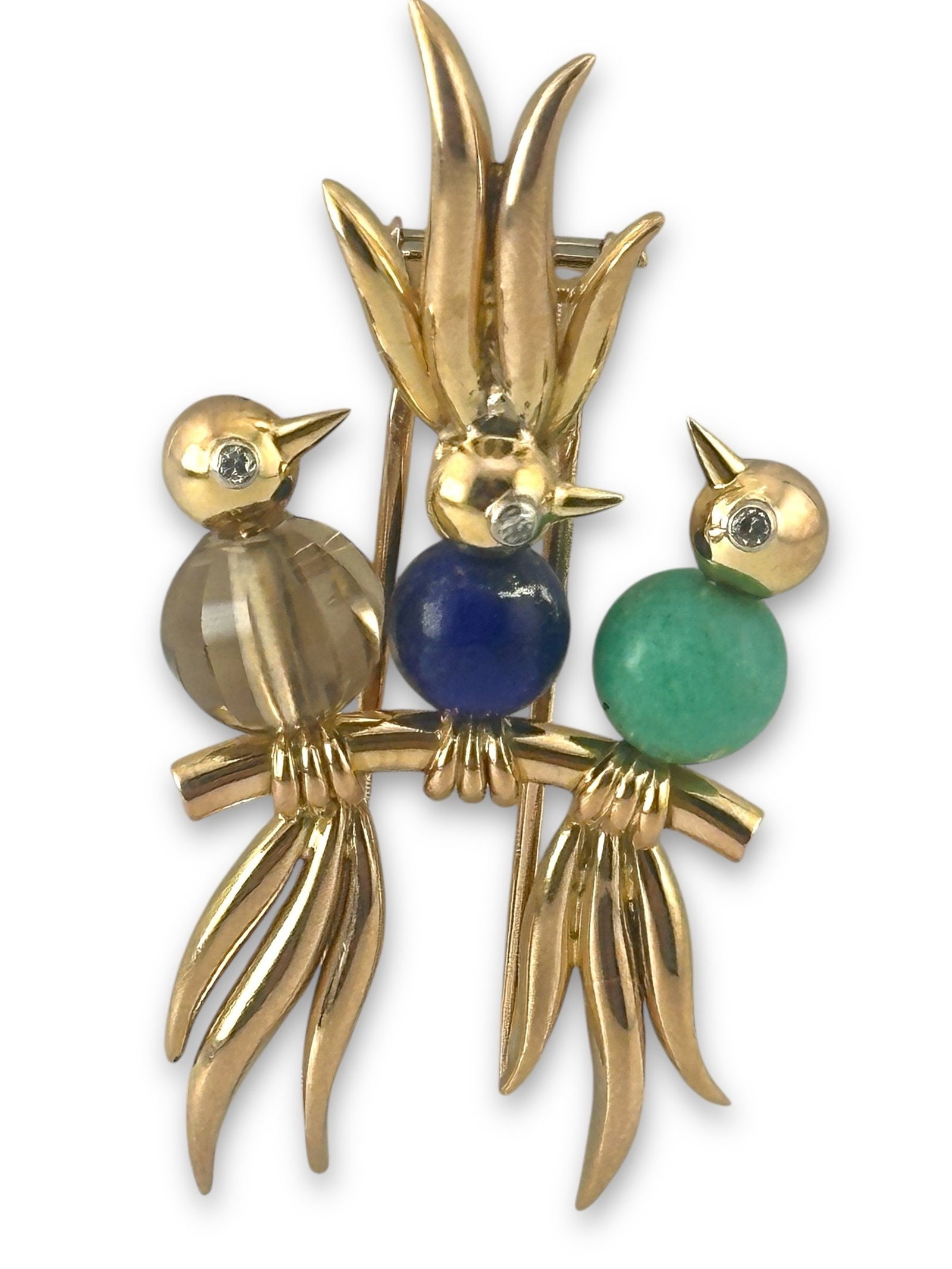 Trio of Birds Diamond-Eyed Brooch: Trio of Birds Diamond-Eyed Brooch in 14K Gold This charming brooch is crafted from 14K yellow gold, featuring three delicately sculpted birds perched gracefully on a slender branch. Each bird is broug