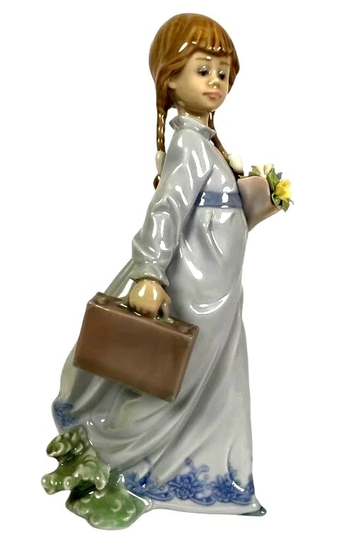 LLADRO SCHOOL DAYS PORCELAIN FIGURINE 7604: LLADRO SCHOOL DAYS PORCELAIN FIGURINE 7604Lladro porcelain figurine titled School Days, model no. 7604. Depicts a young girl in a flowing blue-trimmed dress holding a bouquet of flowers and a school b