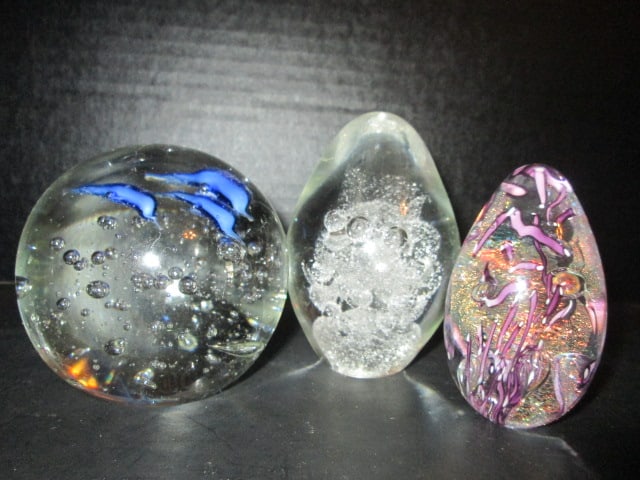 Three Hand Blown Paperweights with Multicolor Controlled Bubble Designs: Purple confetti with bubbles egg shape 3 1/4"h, Egg shape controlled stacked bubbles 4"h, Round controlled bubble and dolphins 3 1/2"dia