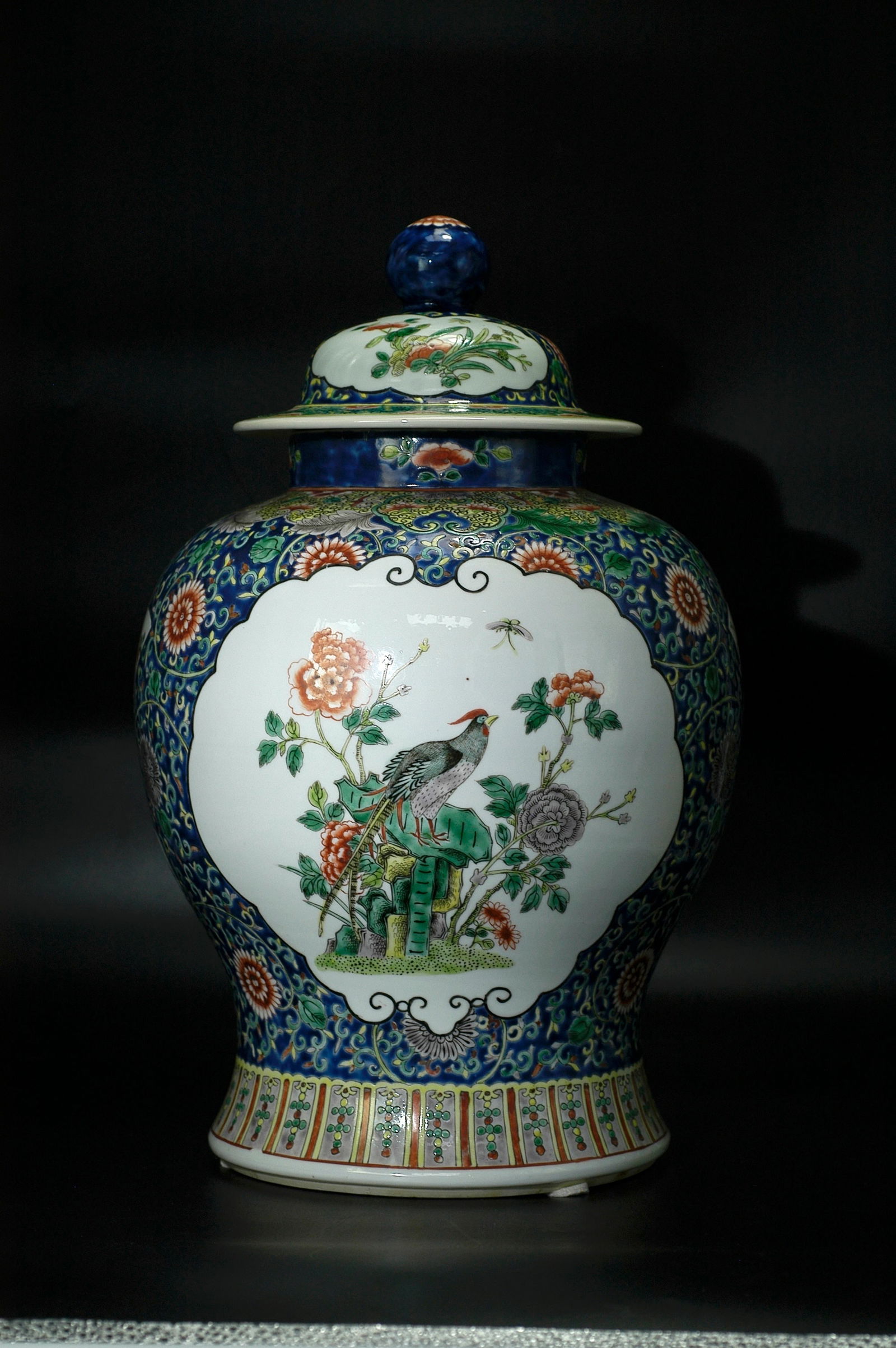 Qing Dynasty Famille Rose Bird-and-Flower Medallion Blue Ground General Jar with Cover: H:41.5cm W:23cm. Period: Qing Guangxu to early Republican period (imitating Kangxi wucai style, folk kiln fine ware). Subject: Sapphire blue ground wucai scrolling floral brocade pattern, ruyi-shaped