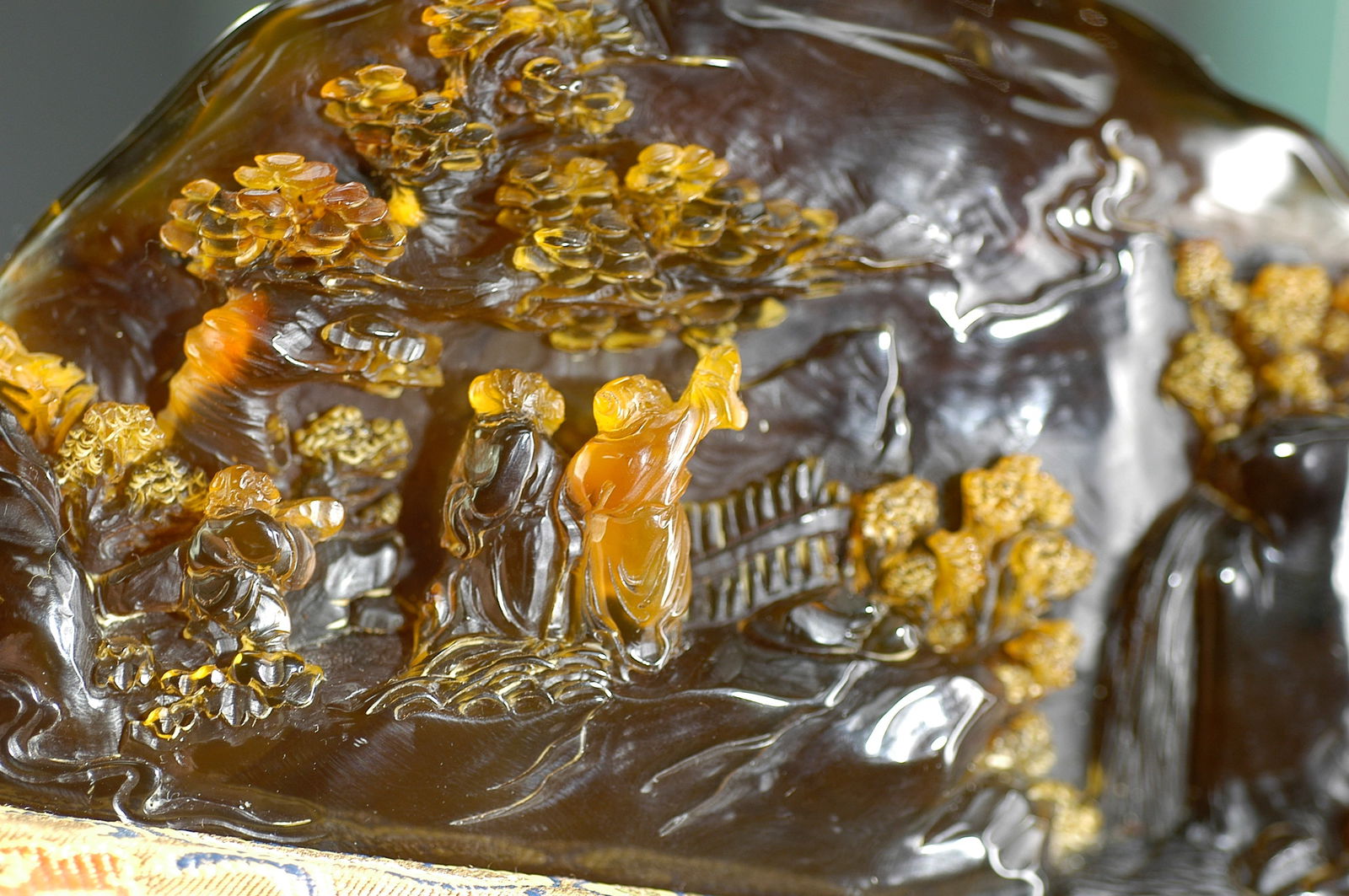 Amber Carved Landscape Figures Narrative Ornament with Modern Cloth-Wrapped Base: H:7.7cm W:16.4cm. Item: Amber Landscape Figure Mountain Carving. Period: Mid Qing Dynasty (18th–19th century). Material: Natural amber (reddish-brown to golden-brown), translucent in quality wit