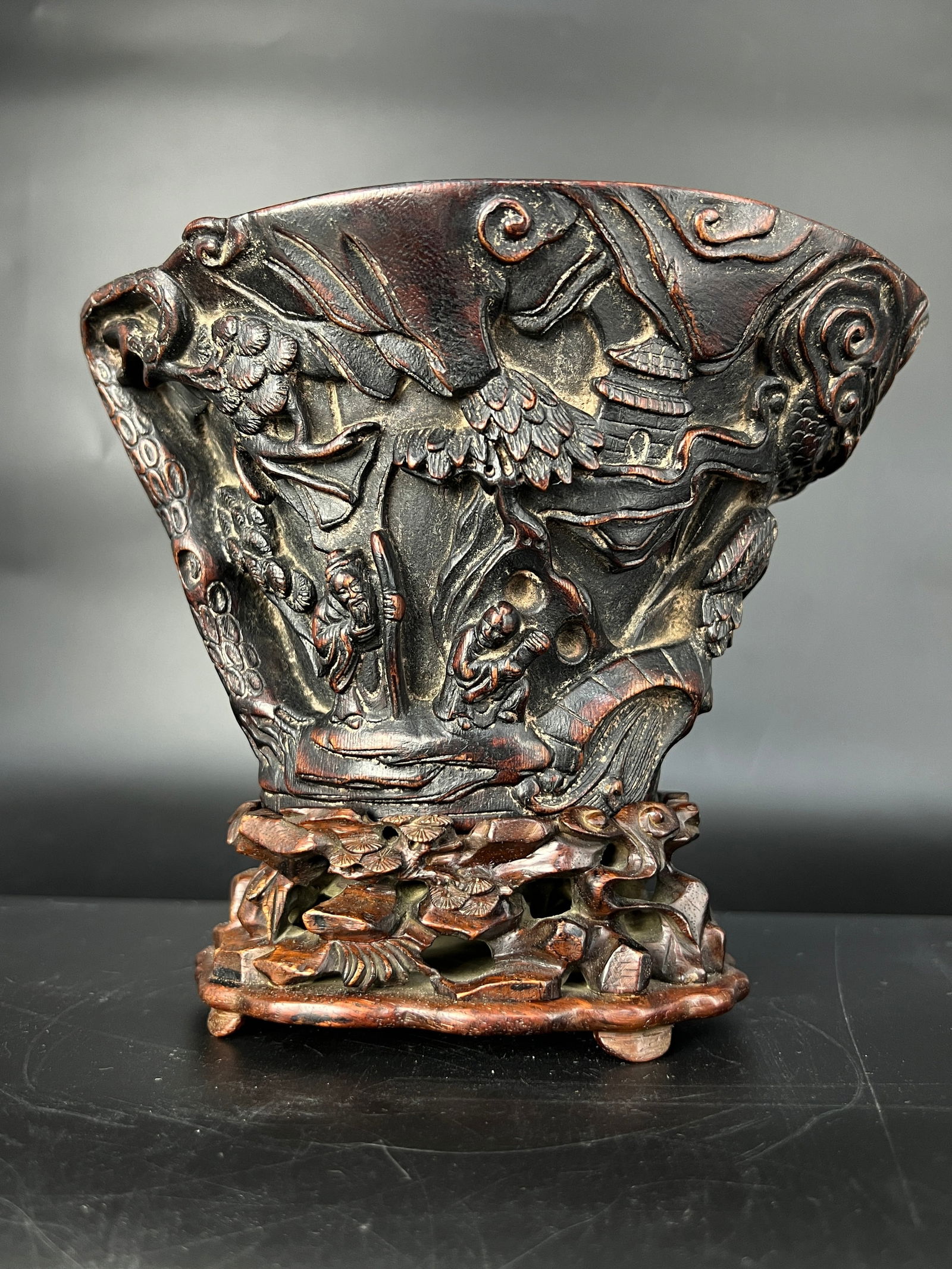 Qing-Republic Period Agarwood Carved Rhinoceros Horn-Style Figural Narrative Cup: H10.5cm W17.2cm. Agarwood Carved Cup with Figural Narrative in the Style of Rhinoceros Horn. Material: Agarwood with hardwood stand. Dating: Mid to late Qing Dynasty. Market Reference Price: RMB