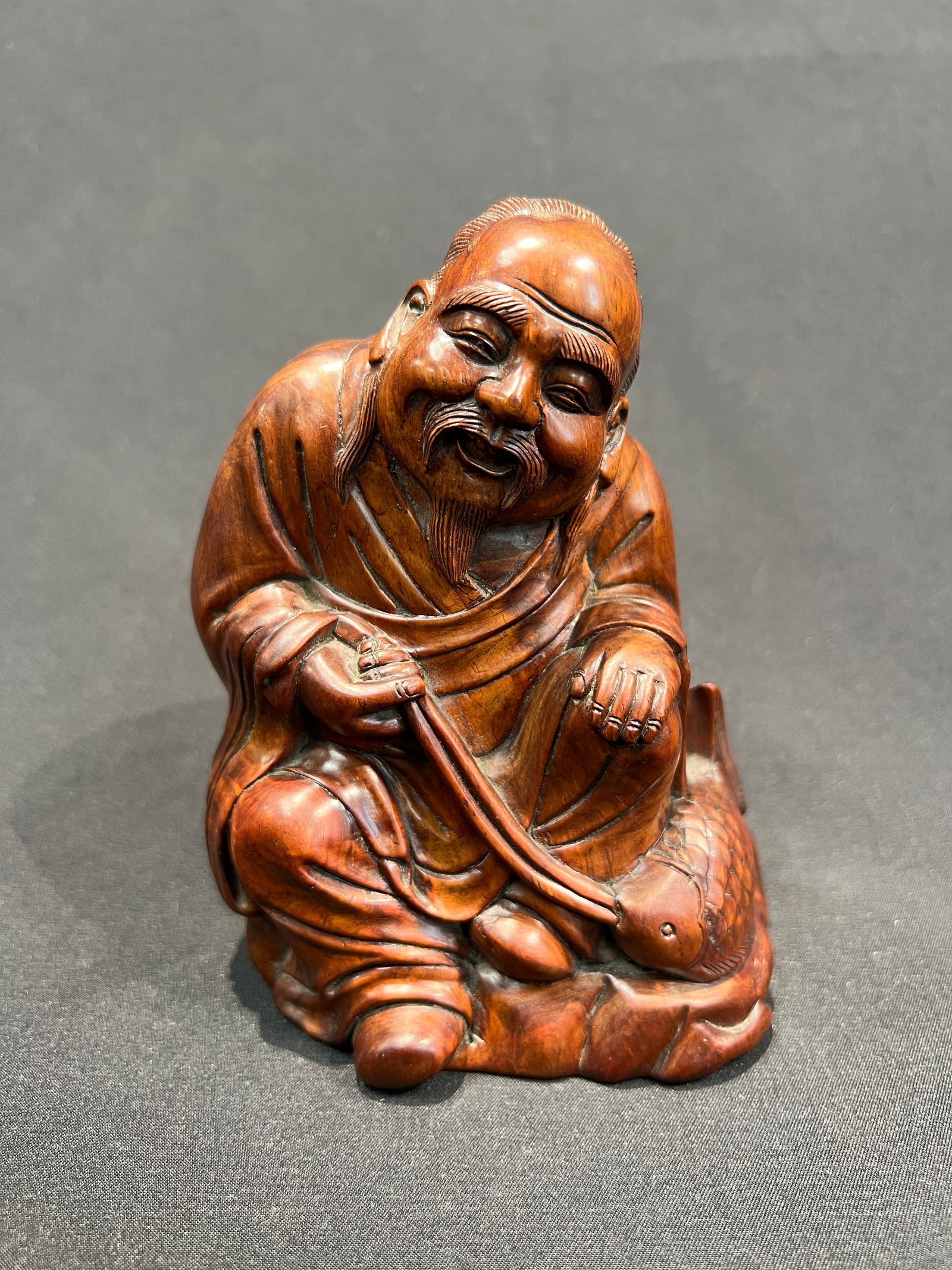 Qing Dynasty Huanghuali Carved 'Fisherman Playing Fish': H13cm W11cm Qing Dynasty/Republic Period Huanghuali Carved Seated Figure 'Fisherman's Gain' (or 'Fisherman Playing with Fish'). Material: Huanghuali wood (or similar premium hardwood) with warm patina