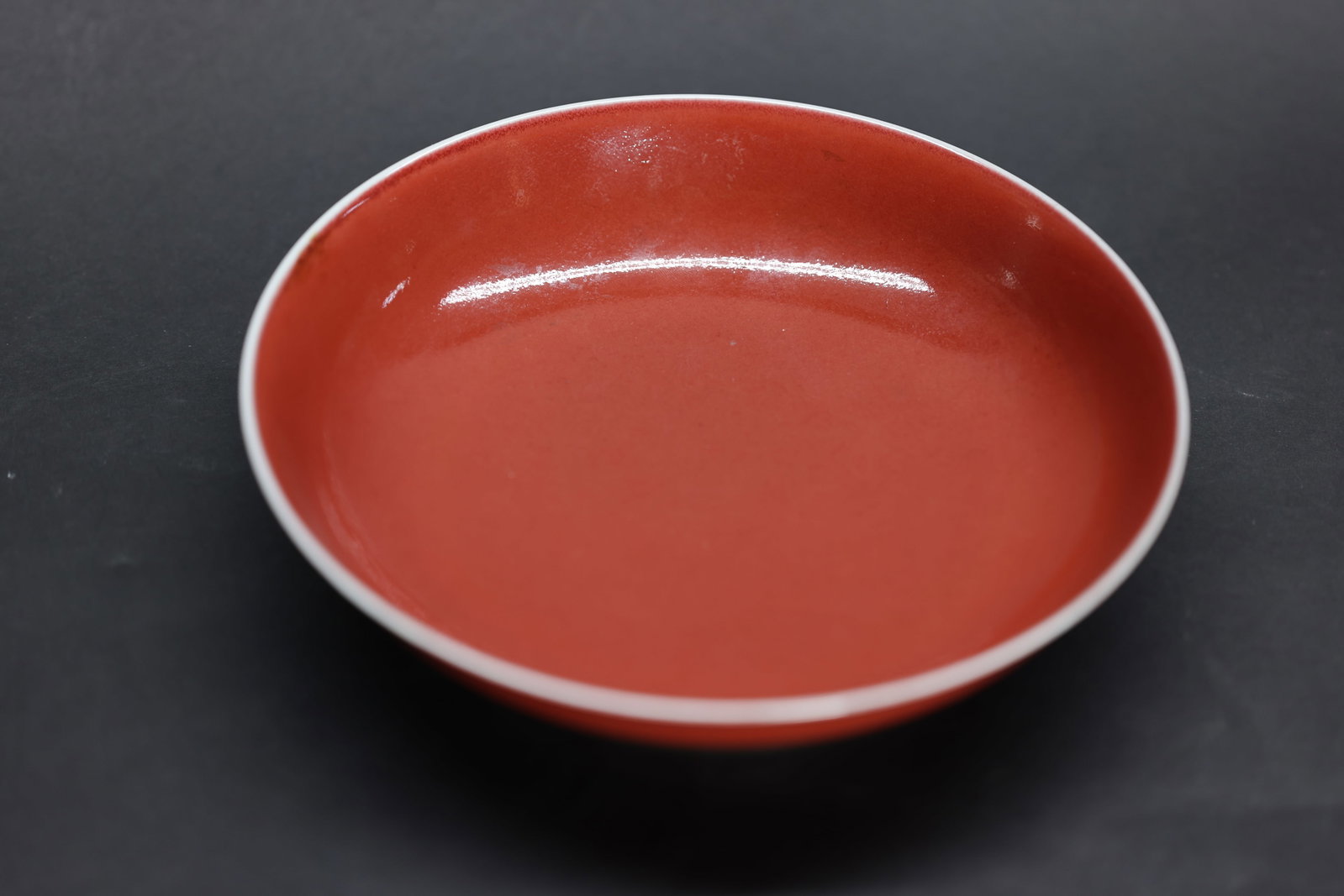 A Sacrificial-Red Dish, Qianlong Mark and Period: Estimated Date: Qianlong Period, Qing Dynasty. An imperial monochrome Jihong (sacrificial red) glazed dish bearing the Qianlong reign mark.Attribution: The dish is finely potted with shallow rounded s