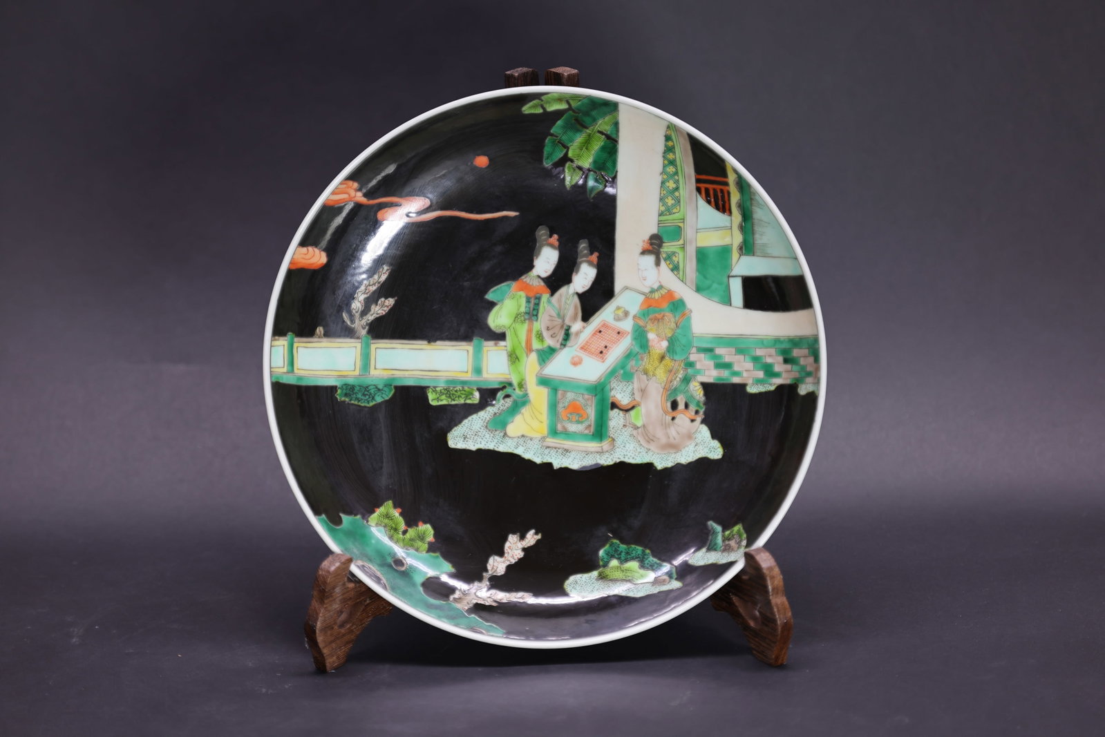 A Rare Large 'Famille-Noire' 'Ladies' Dish, Qing Dynasty: Estimated Date: Late Qing Dynasty. A black-ground Wucai enamel porcelain display charger decorated with court ladies.Attribution: The charger is of shallow, wide-rimmed form and decorated on the inter