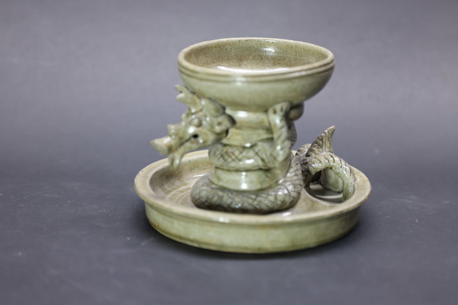 A 'Yue' Celadon 'Dragon' Stem Cup, Six Dynasties to Tang Dynasty: Estimated Date: Jin Dynasty. Attributed to the Yue kilns as a celadon dragon-form pedestal offering cup created for the scholar's studio or as a ceremonial display piece.Attribution: The vessel is cov