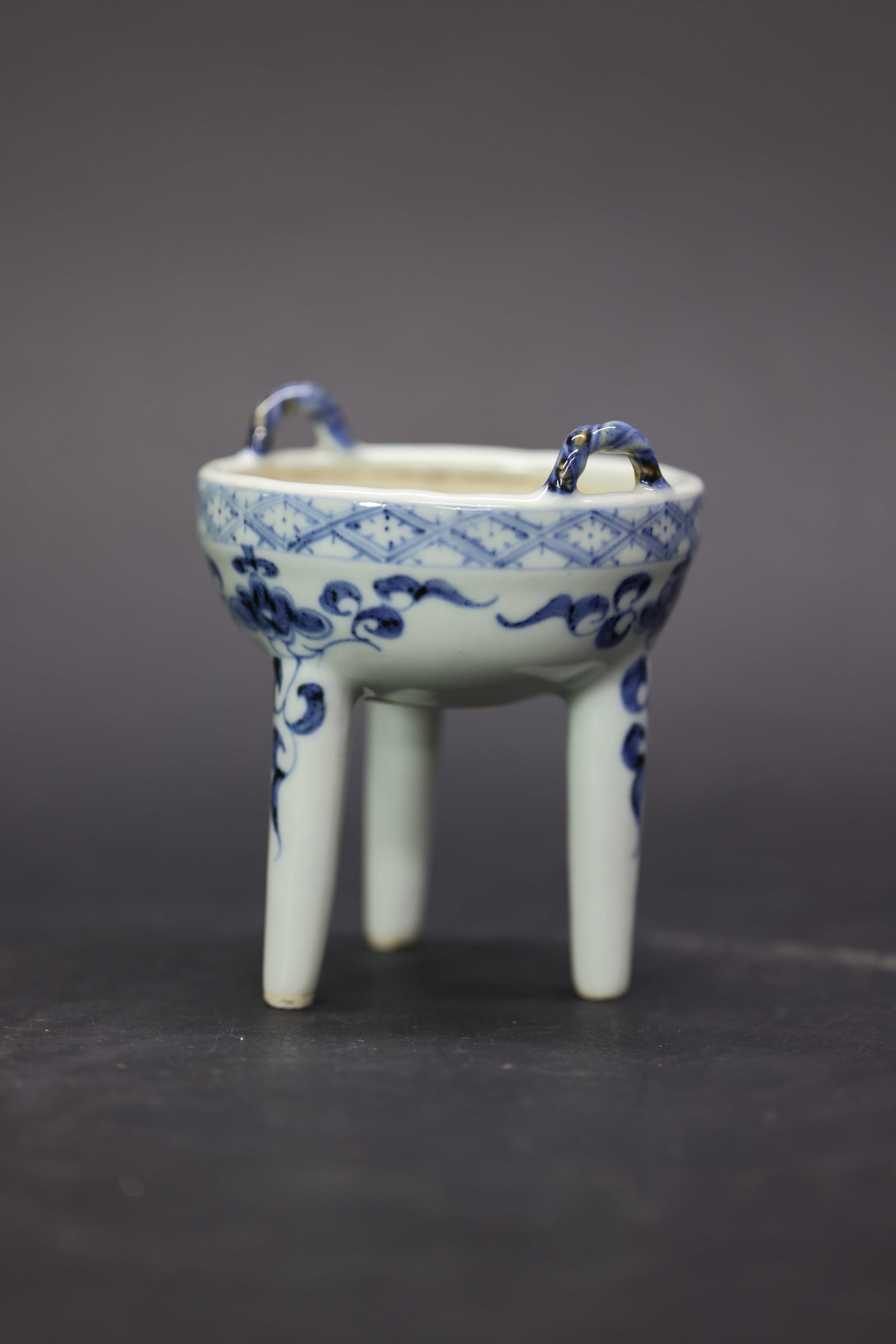 A Rare Small Blue and White 'Interlocking Floral' Ribbon-Handled Tripod Censer, Ming Dynasty: Estimated Date: Mid to Late Ming Dynasty. A blue and white tripod ge-form scholar's incense burner (qinlu) from a private kiln.Attribution: The incense burner is modeled after the archaic bronze ge ve