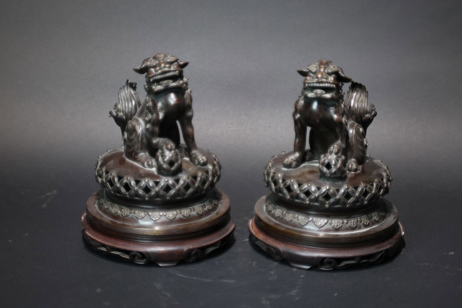 A Pair of Bronze 'Foo Dogs' Incense Burners, Qing Dynasty: Estimated Date: Late Qing Dynasty. A pierced brass lion censer and scholar's desk ornament with original hardwood stand.Attribution: Cast in yellow brass, the censer is modeled as two playful lions, o